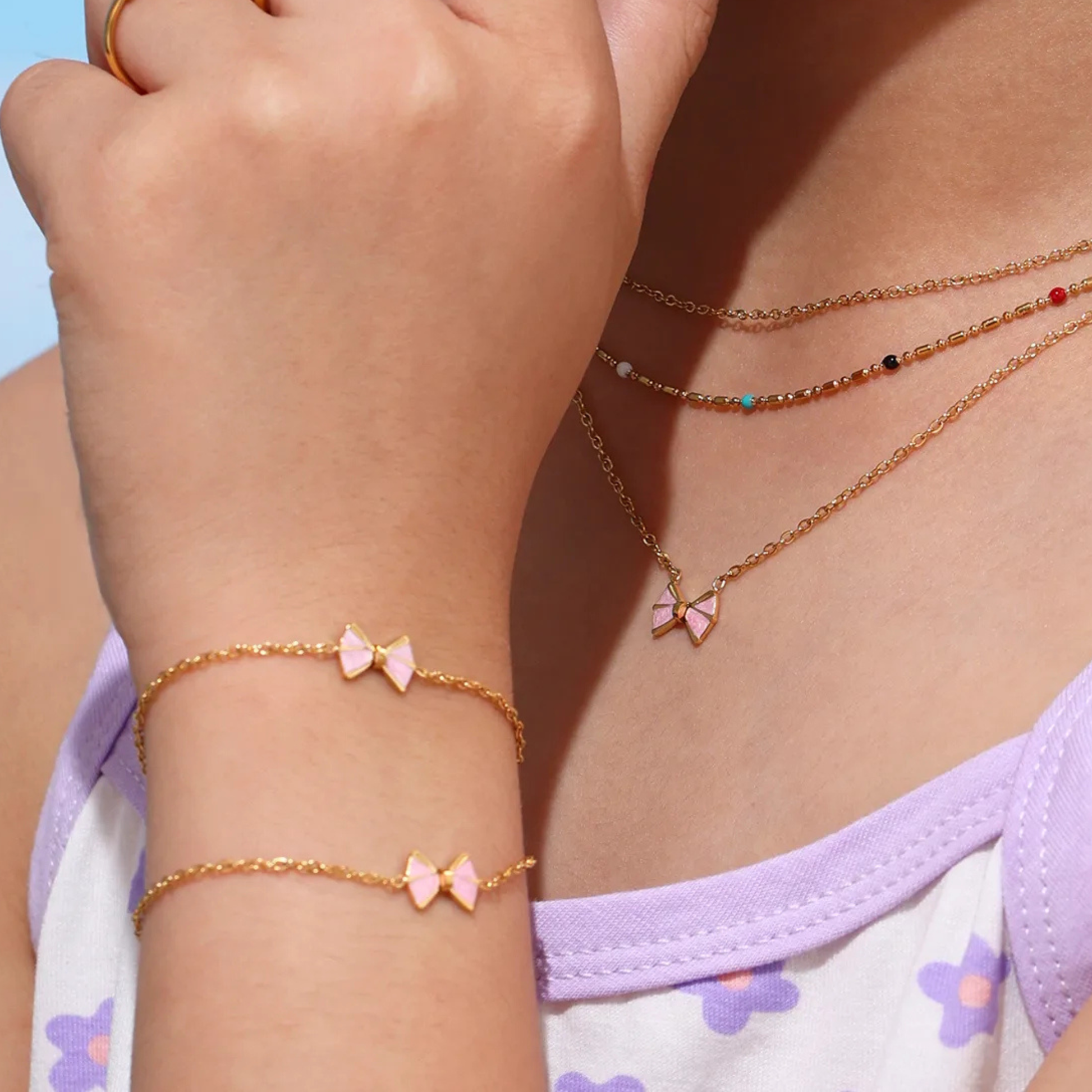 Close-up of a person wearing gold necklaces and bracelets with pink bow details.