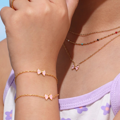 Close-up of a person wearing gold necklaces and bracelets with pink bow details.