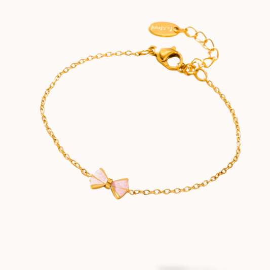 Gold bracelet with a pink bow charm on a white background