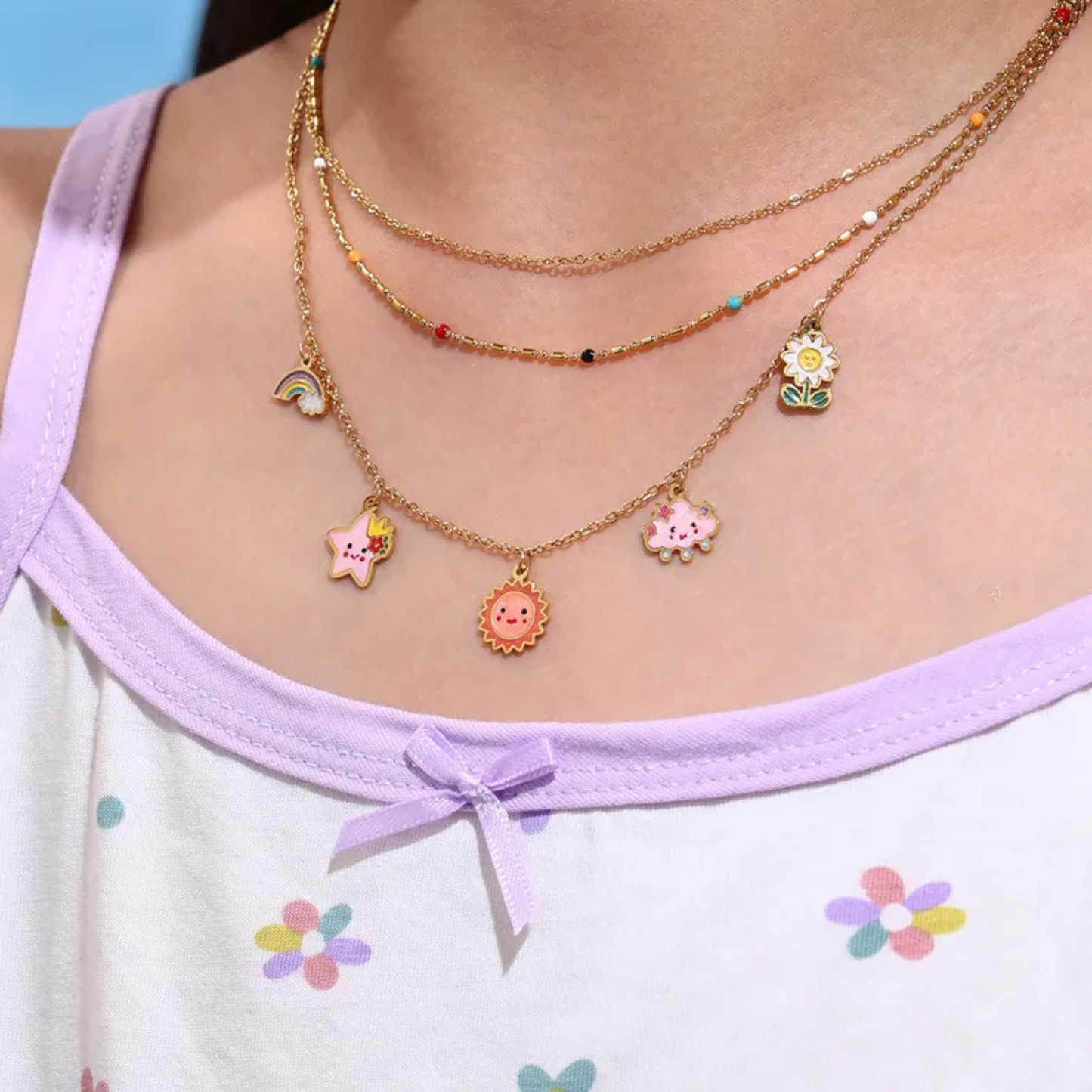 Necklace with colorful charms worn by a person in a light purple top with floral patterns.