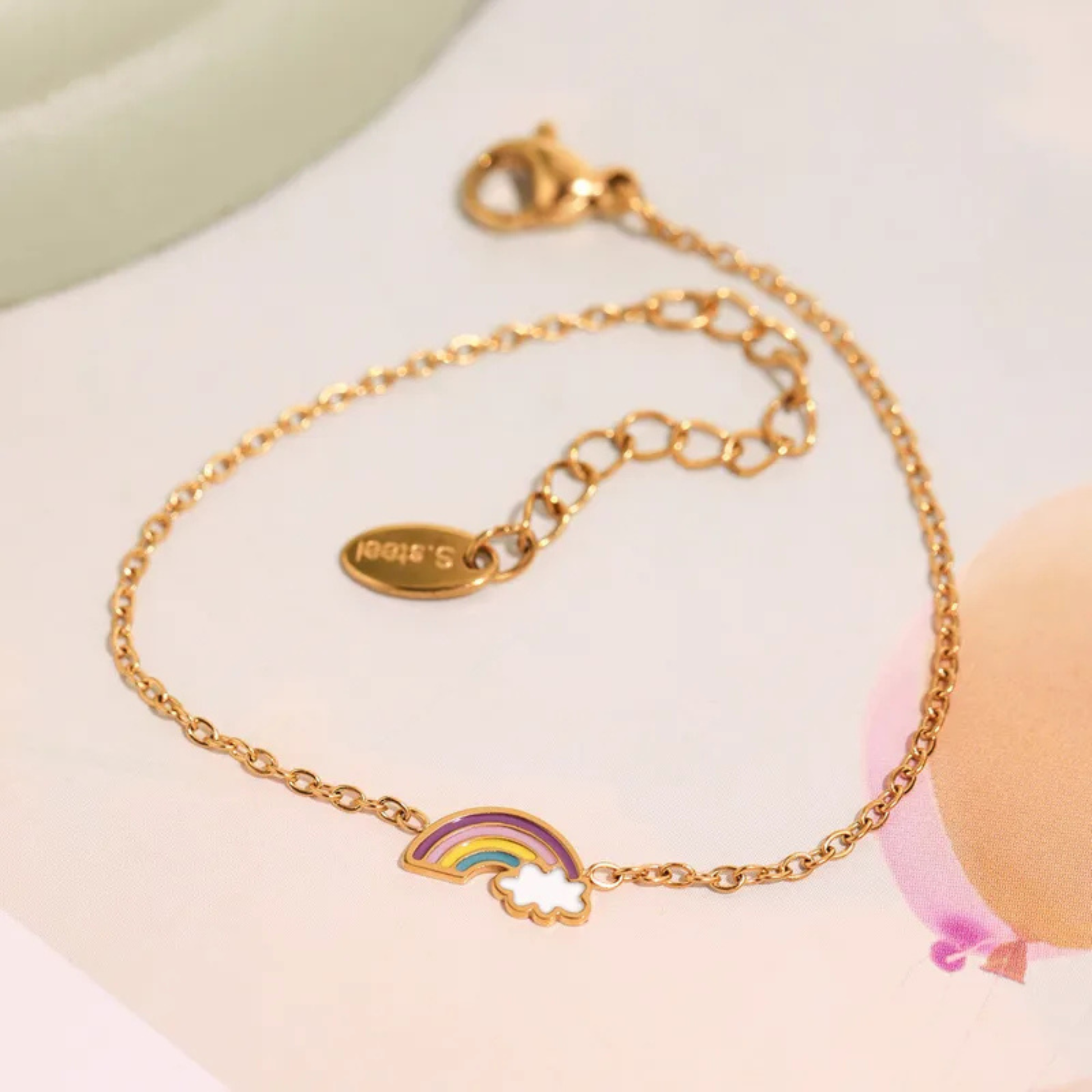 Gold bracelet with rainbow and cloud charm on a light background