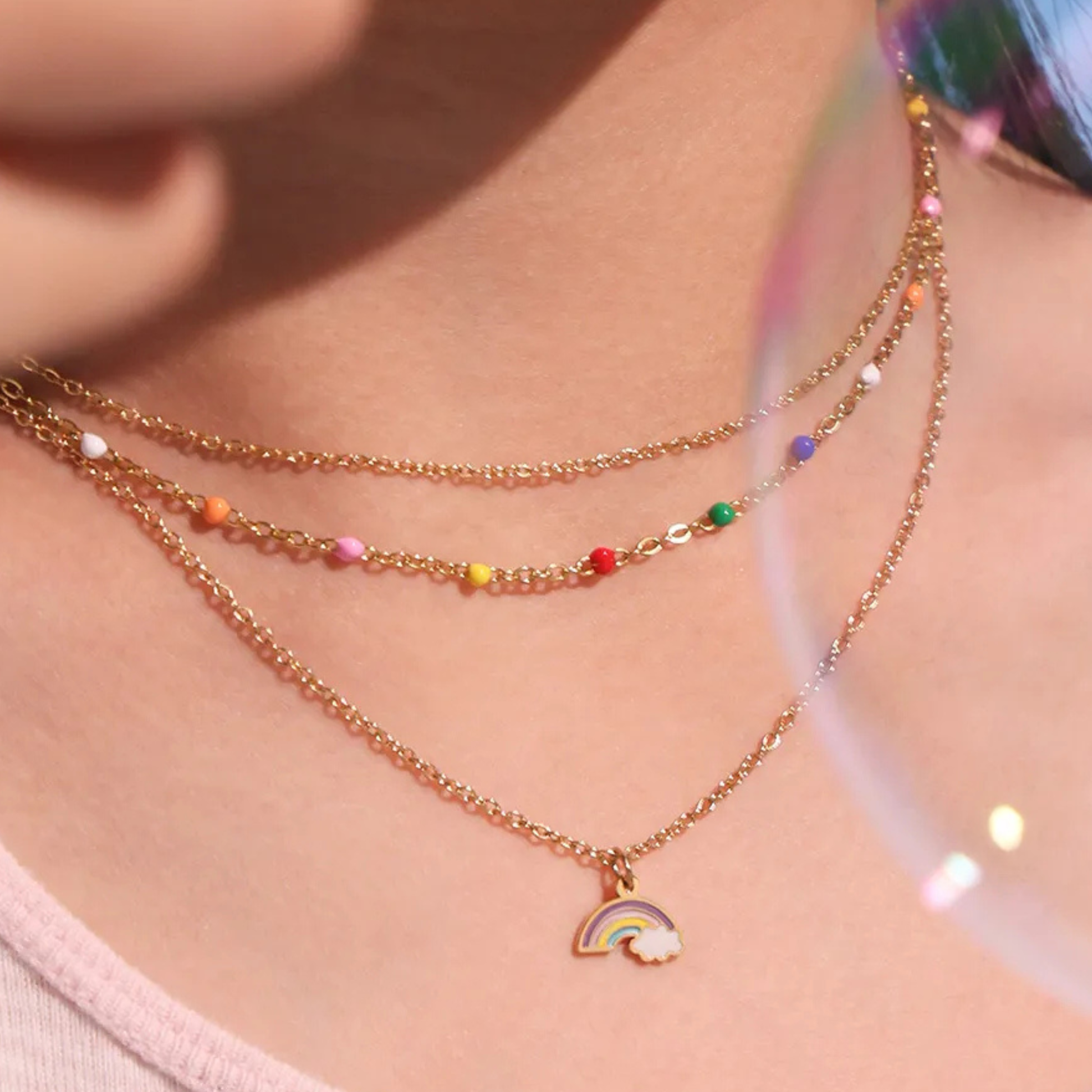 Necklace with rainbow charm worn by a person on a light pink background