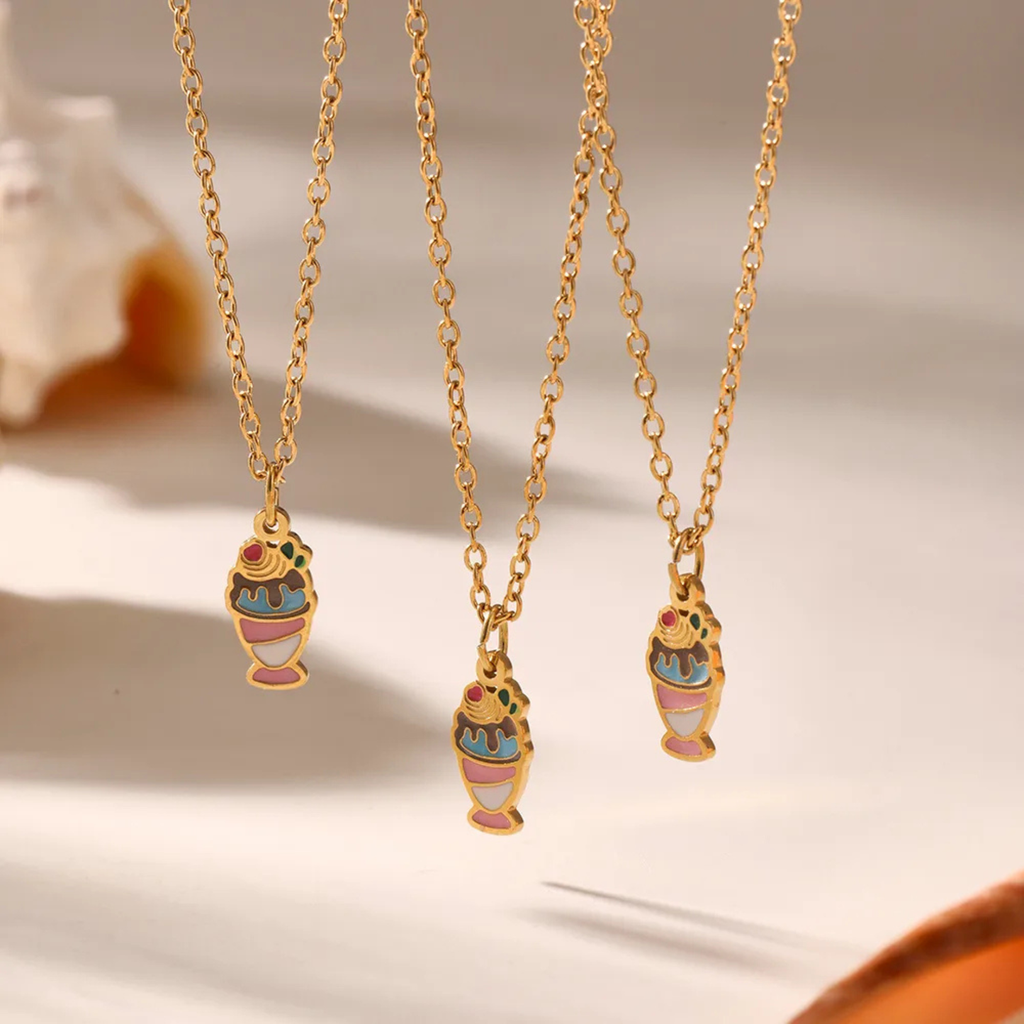 Three gold necklaces with colorful pendant charms on a neutral background