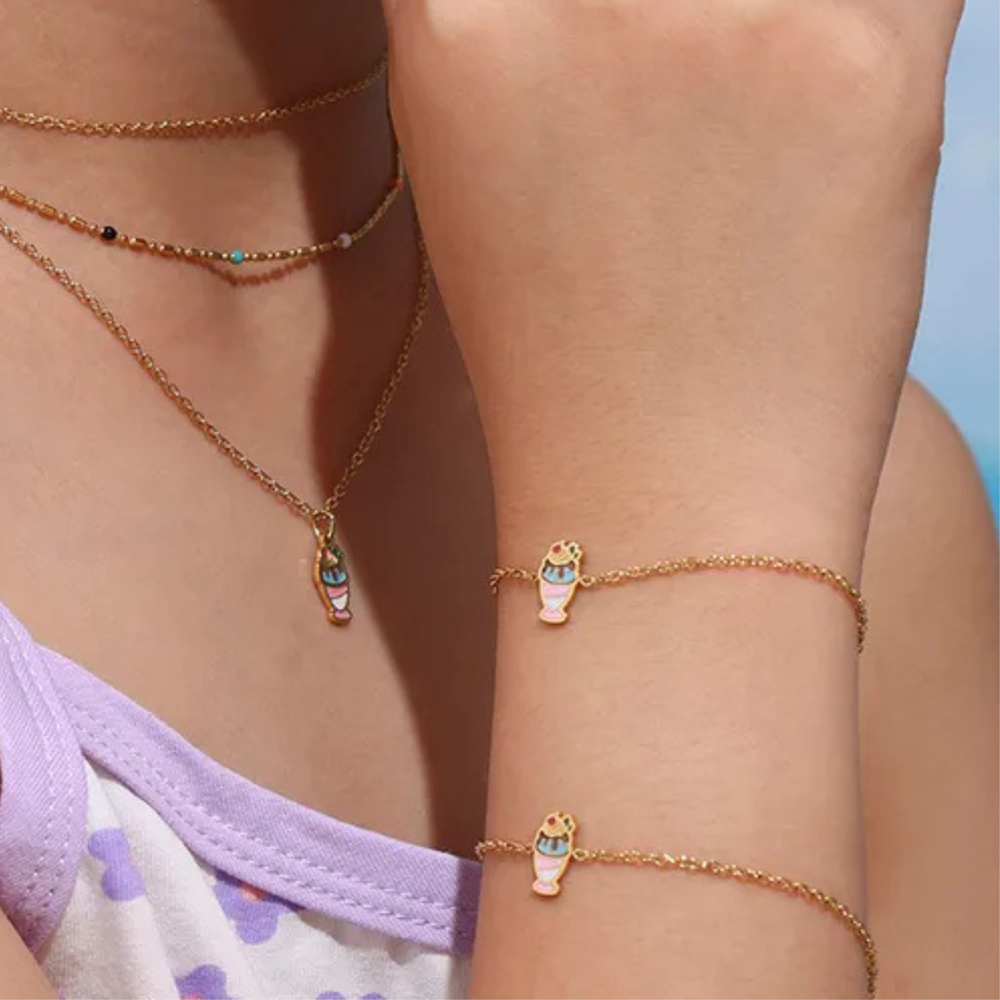Close-up of a person wearing gold necklaces and bracelets with colorful pendants against a light blue background.