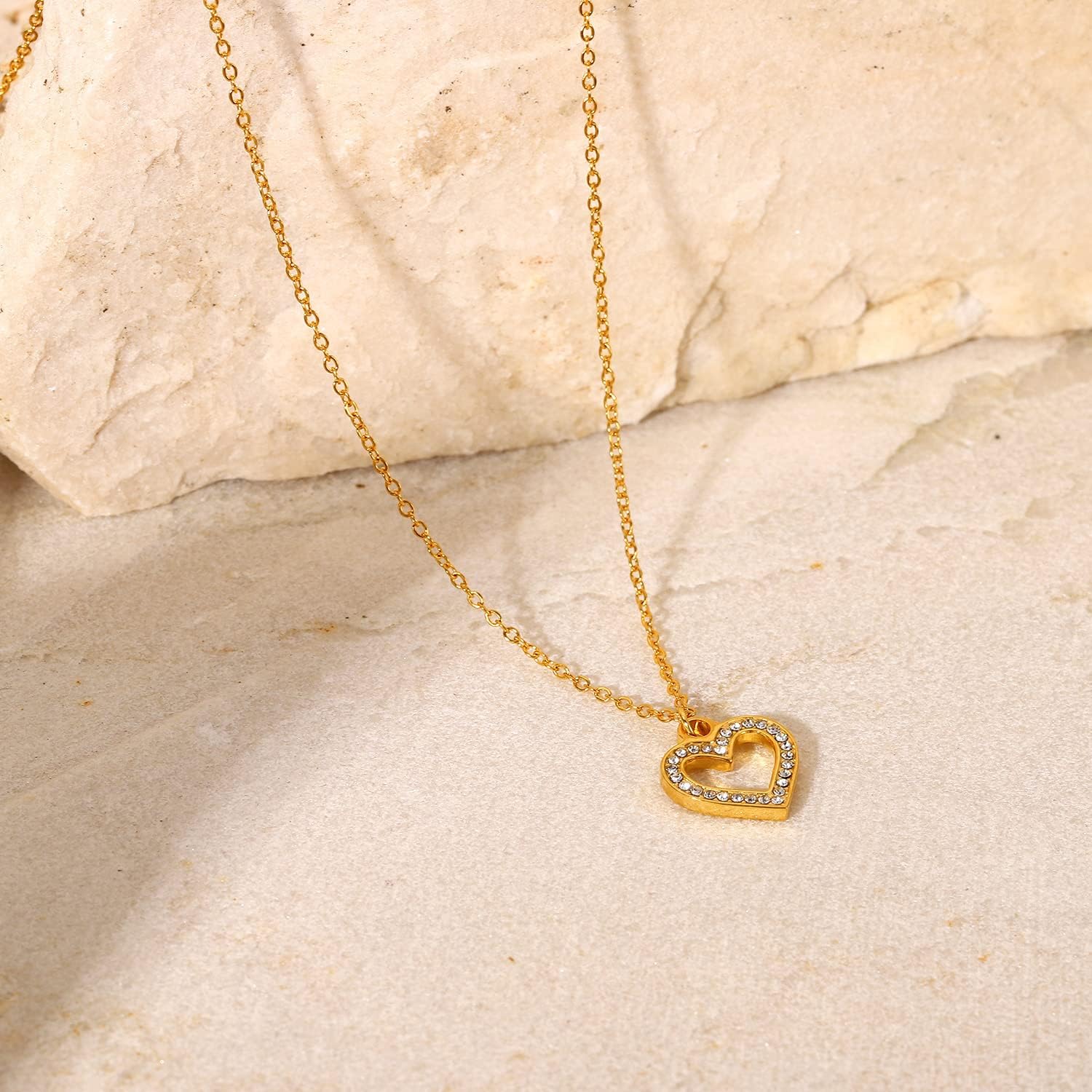 Gold necklace with a heart-shaped pendant on a beige stone surface