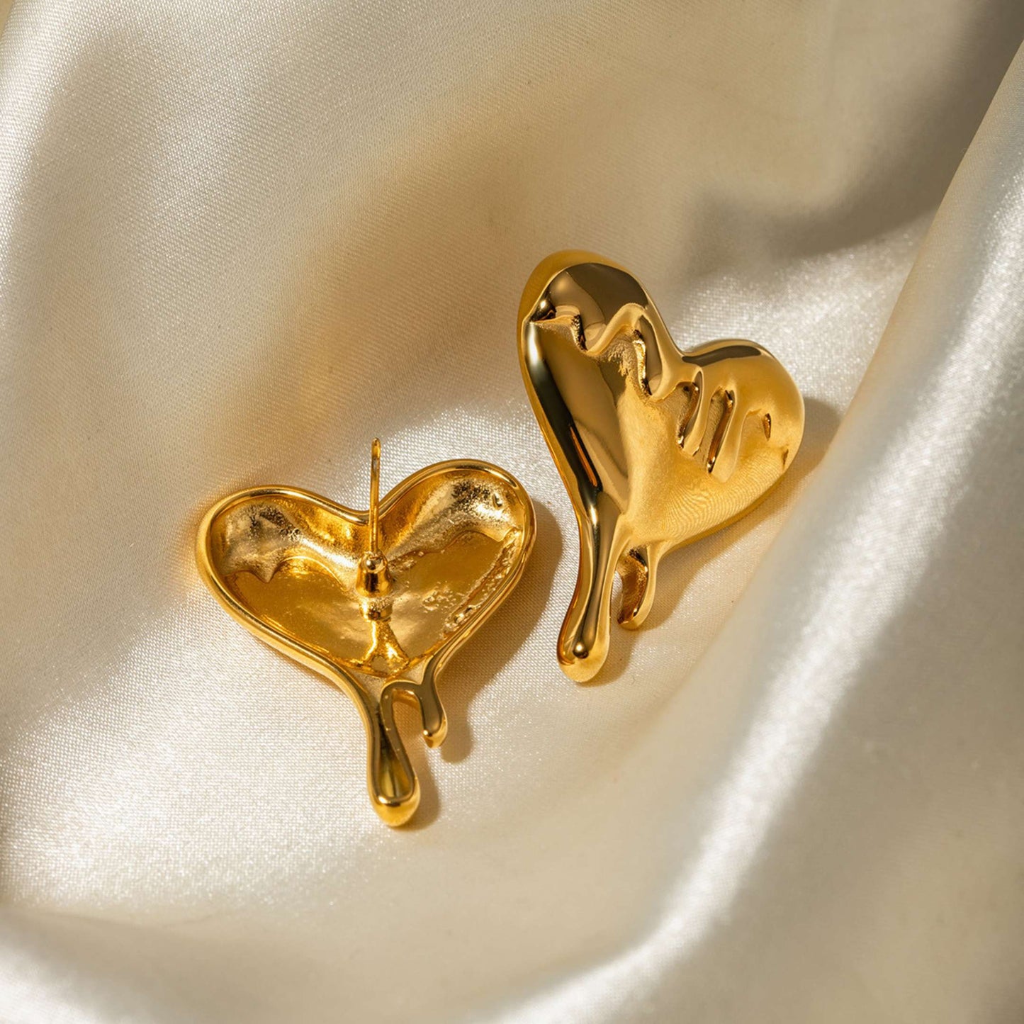 Gold drip heart-shaped earrings on a satin surface