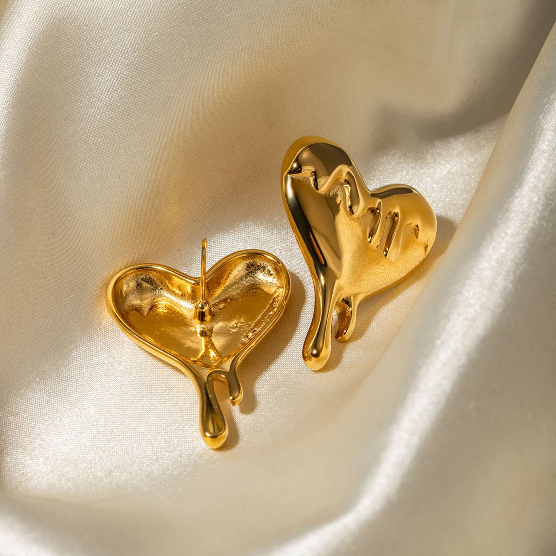 Gold drip heart-shaped earrings on a satin surface