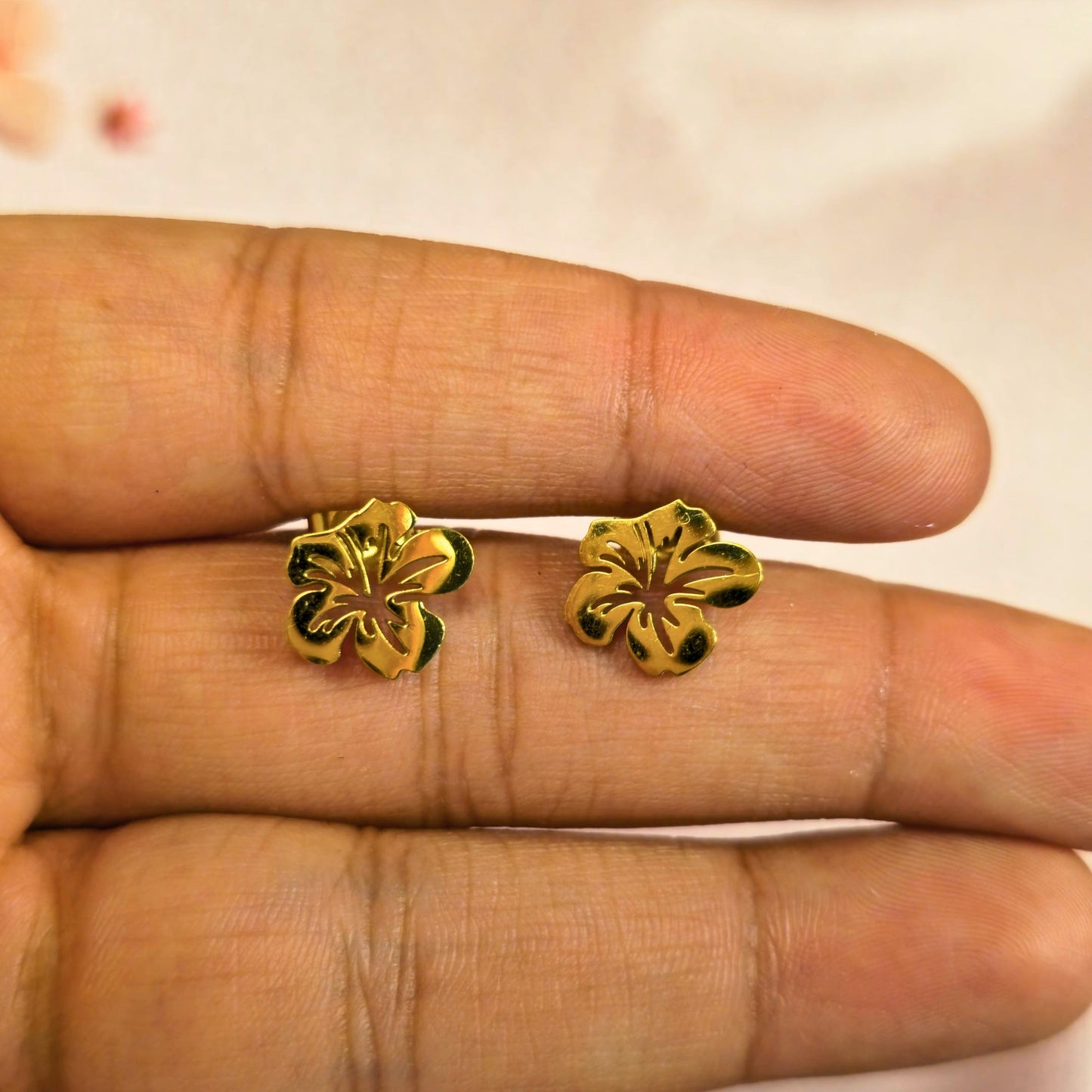 Gold floral earrings held between fingers against a neutral background