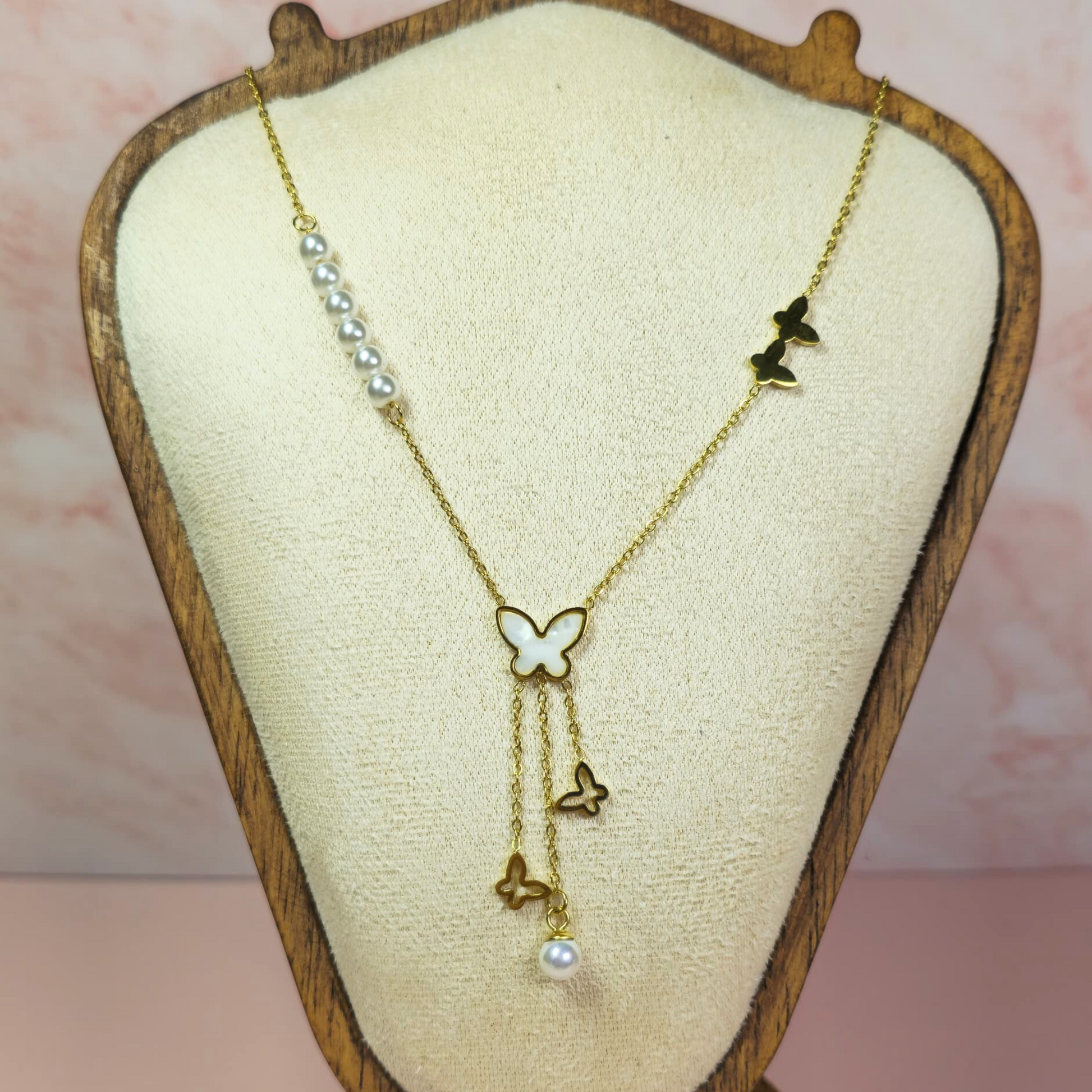 Gold necklace with butterfly and pearl details on a wooden display