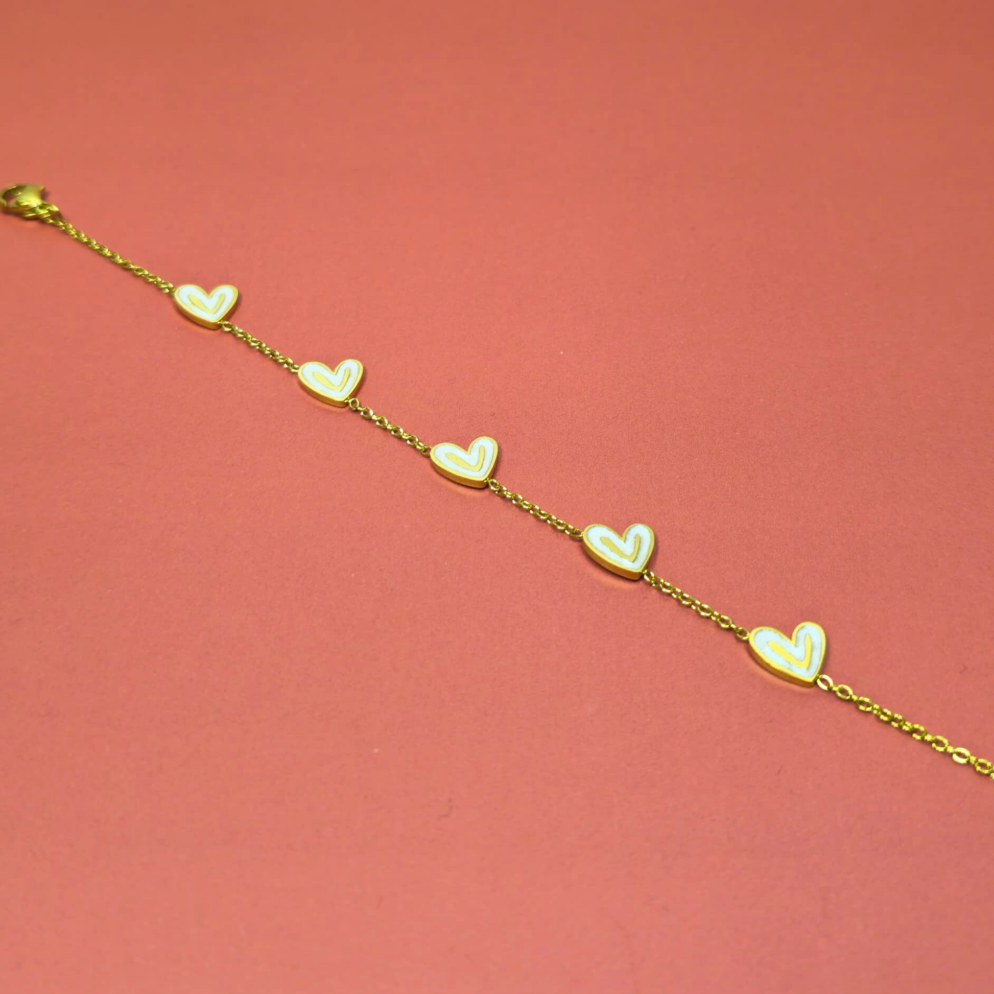 Gold bracelet with heart-shaped charms on a pink background