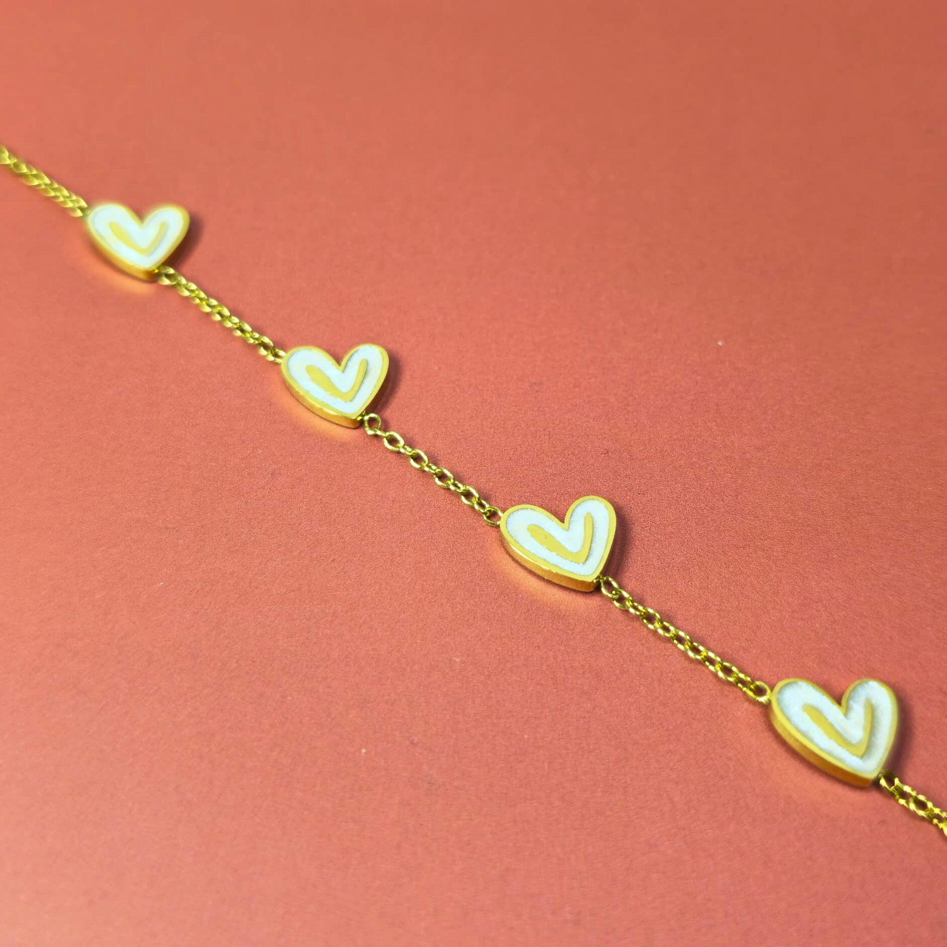 Gold bracelet with heart-shaped charms on a pink background
