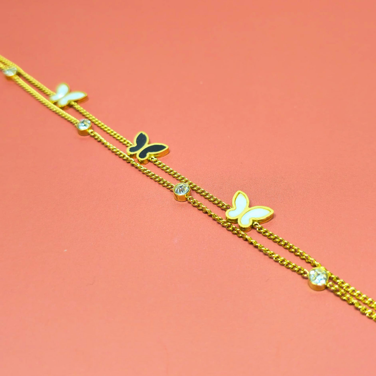 Gold bracelet with butterfly charms on a pink background