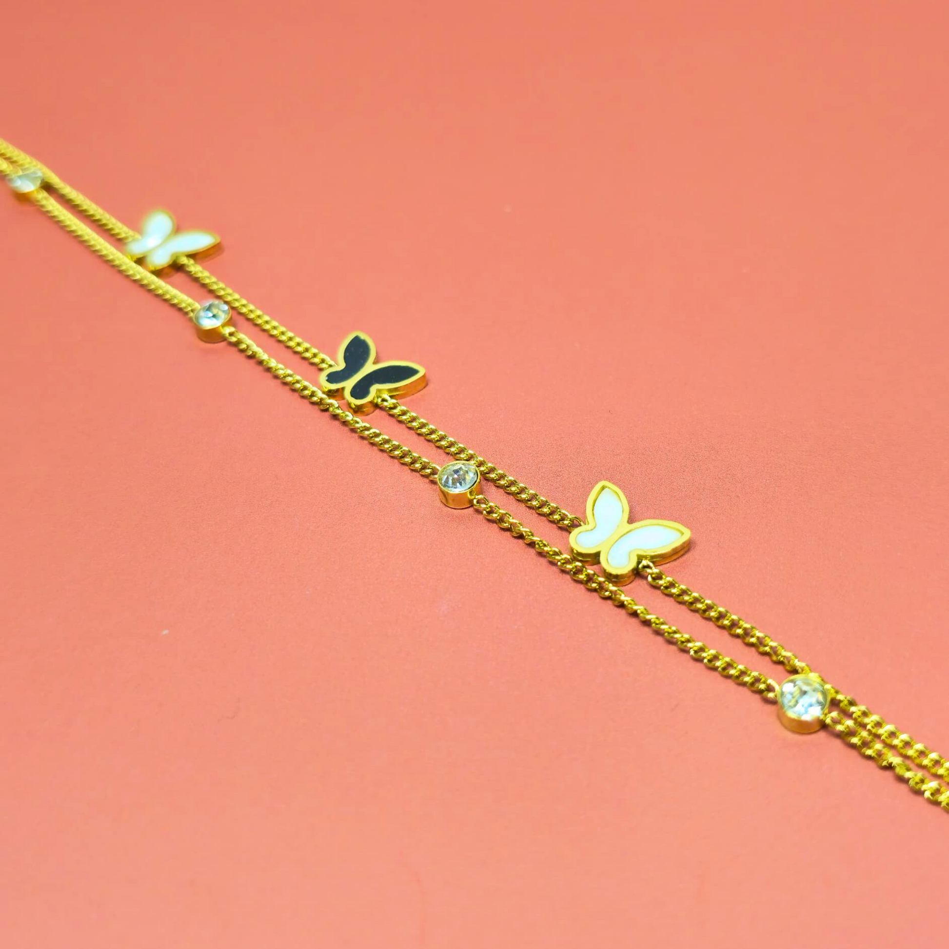 Gold bracelet with butterfly charms on a pink background