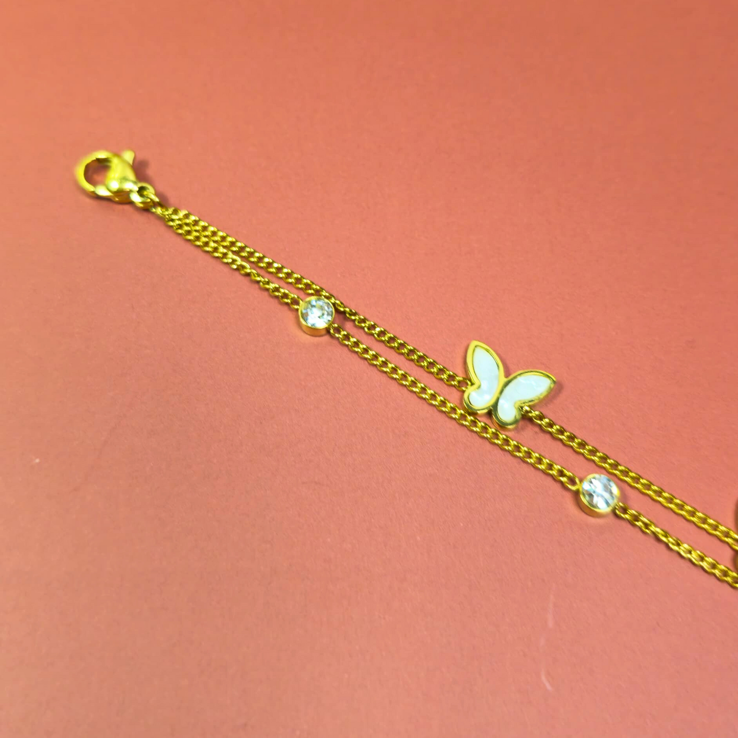 Gold bracelet with a butterfly charm on a pink background