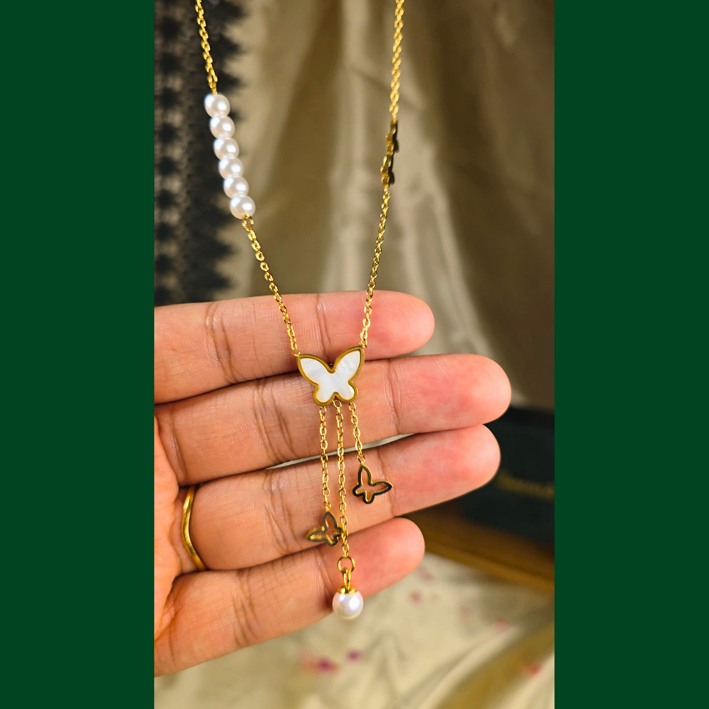 Gold necklace with butterfly and pearl pendants held in a hand against a blurred background