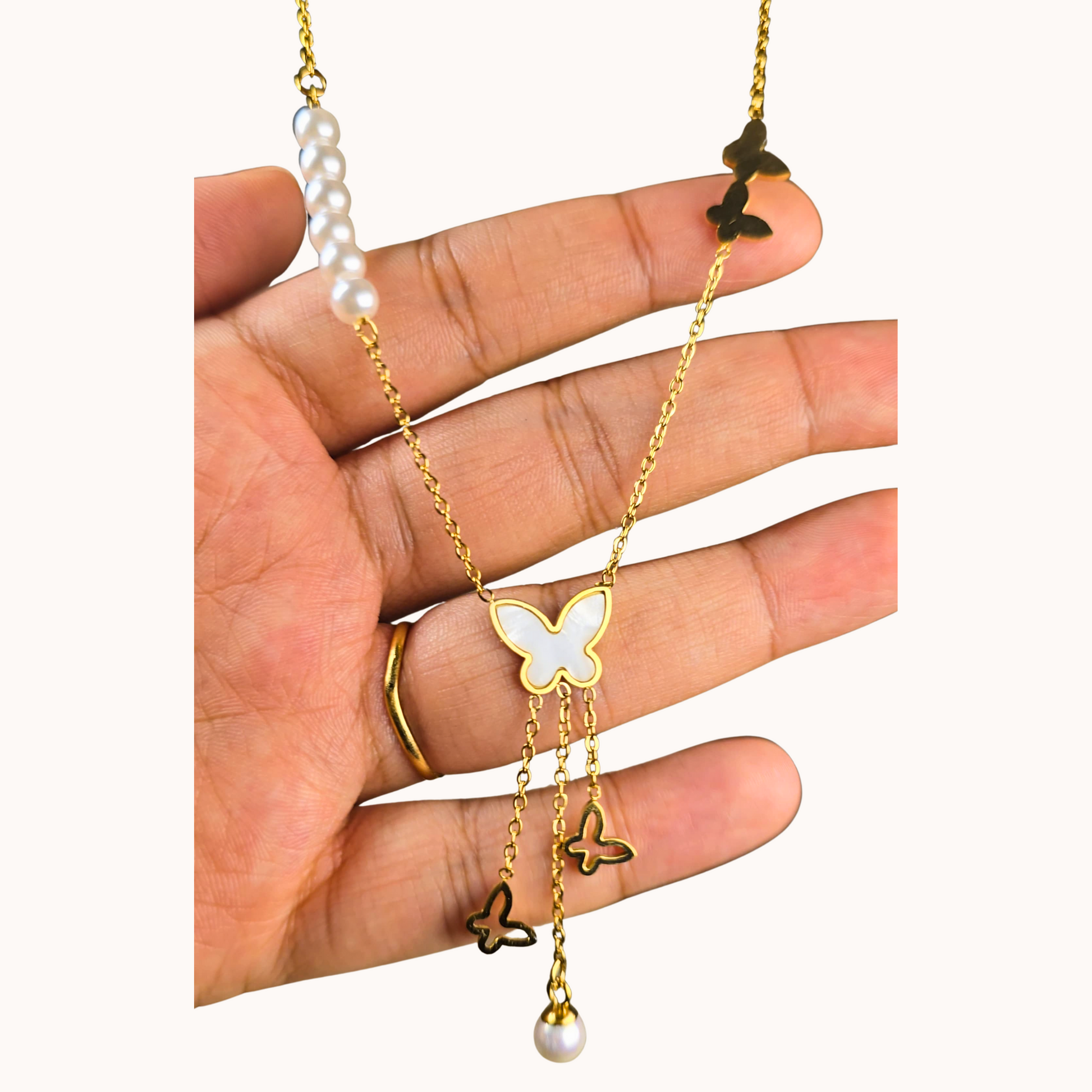 Gold necklace with butterfly pendants and pearl beads held by a hand on a white background