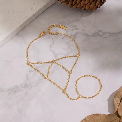 Gold chain necklace on a marble surface with a pine cone and leaf.