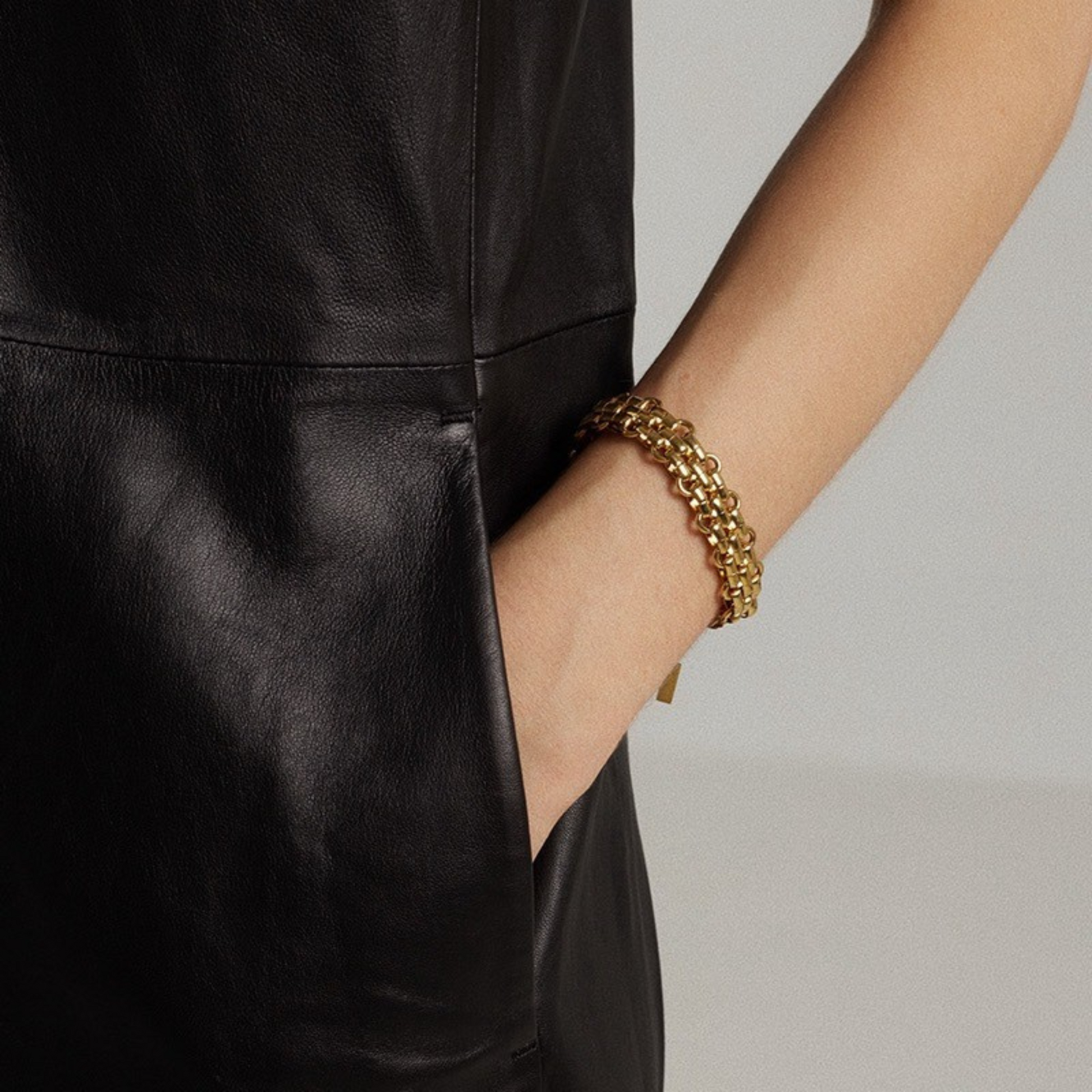 Person wearing a gold bracelet on a plain background