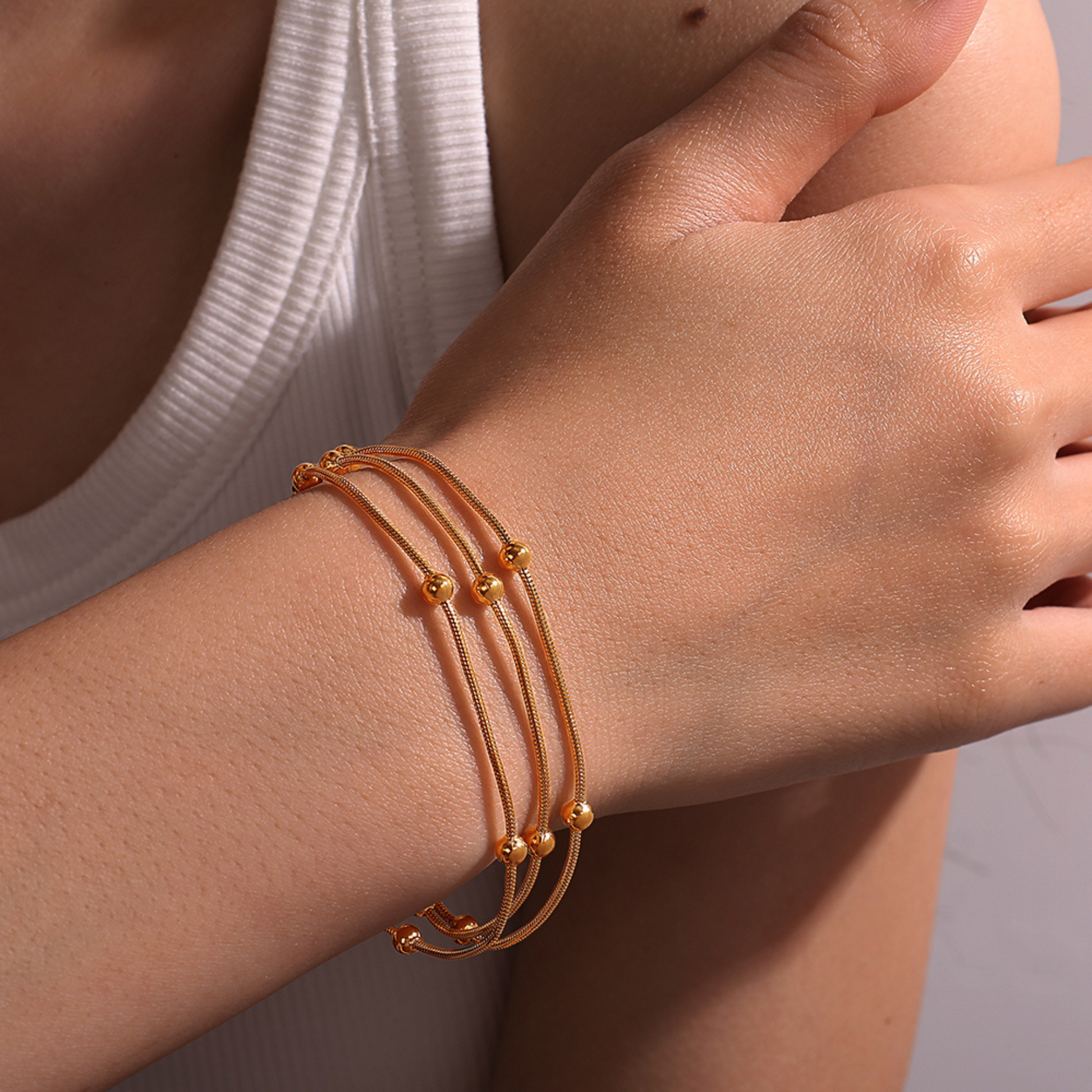 Close-up of a wrist wearing multiple gold bracelets on a neutral background