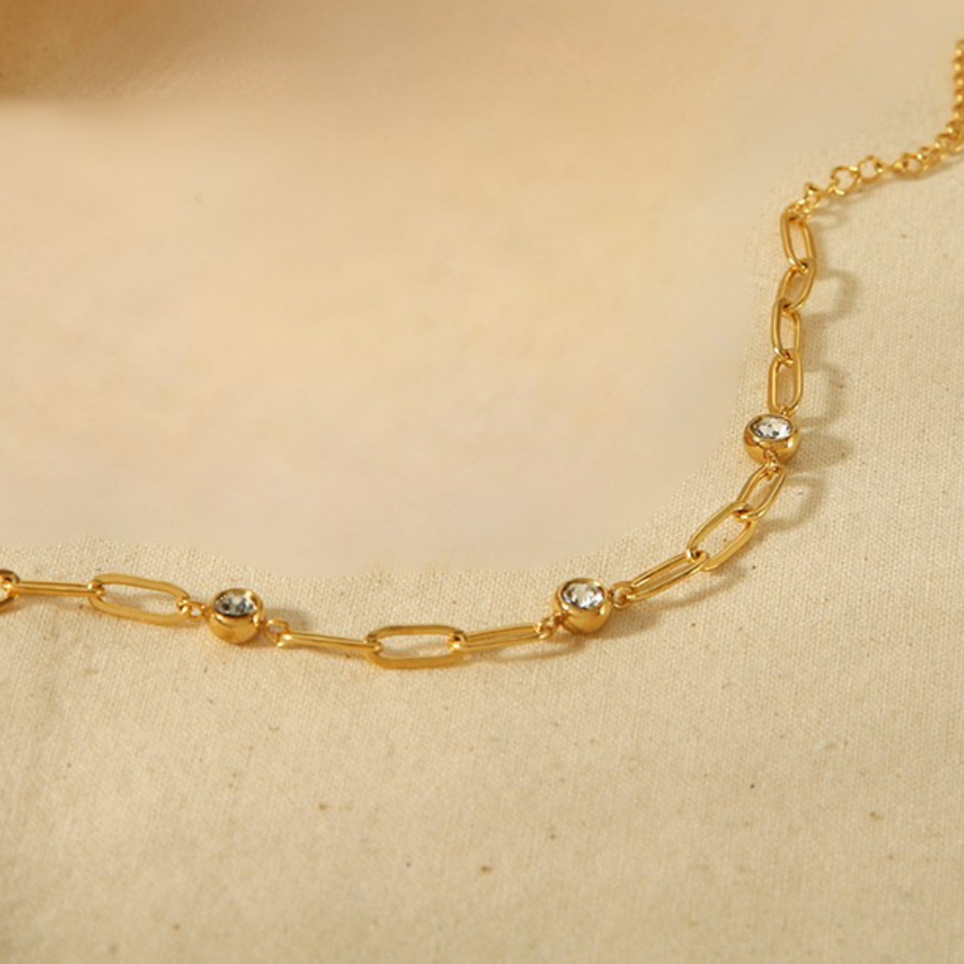 Gold chain necklace with small diamonds on a beige background