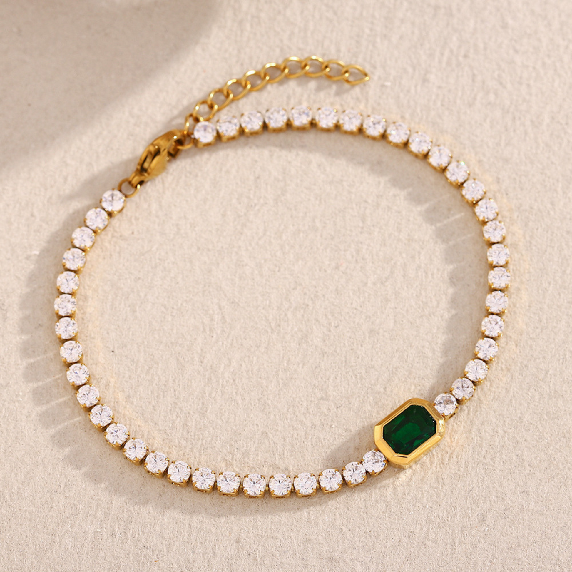 Gold bracelet with green gemstone on a beige background