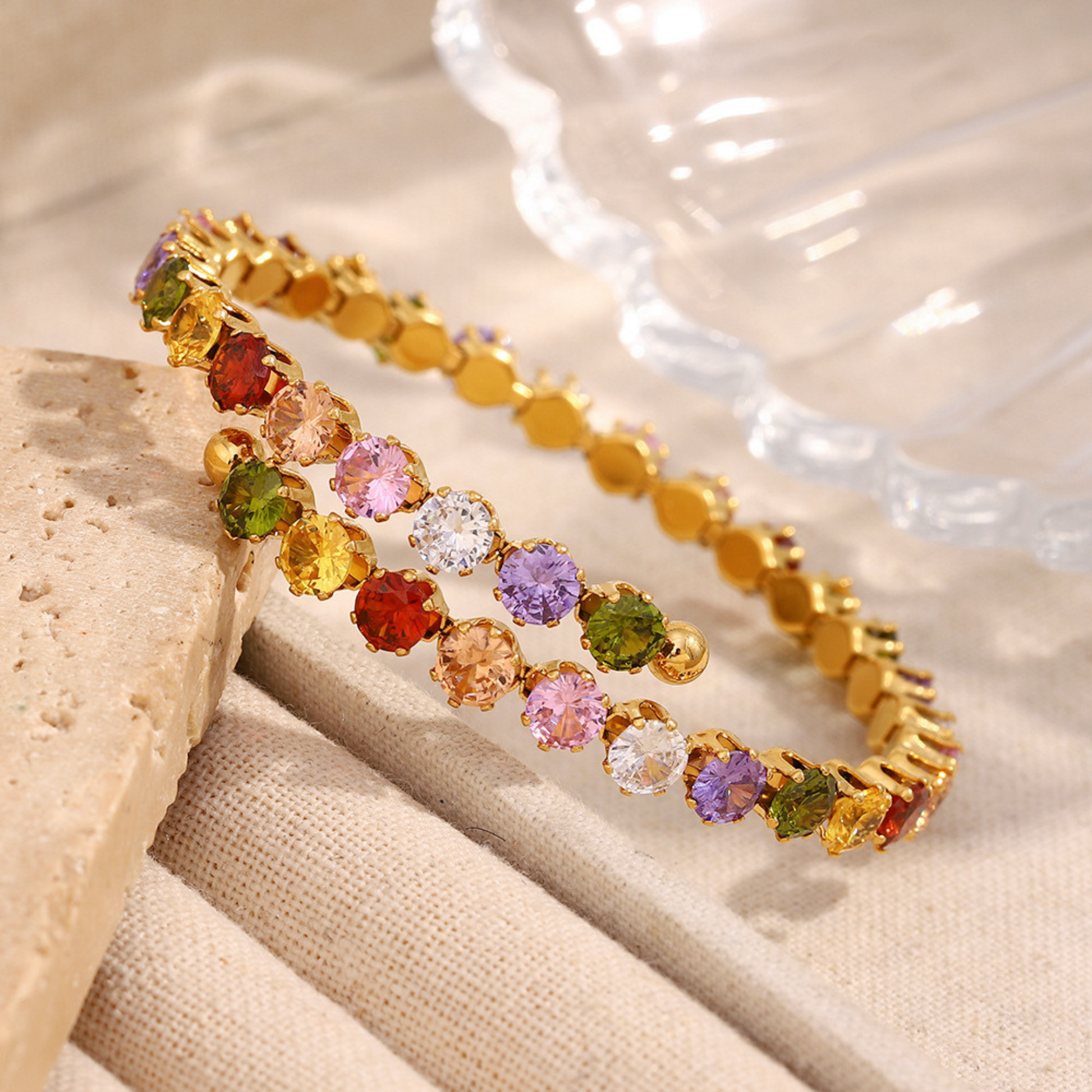 Gold bracelet with multicolored gemstones on a beige surface