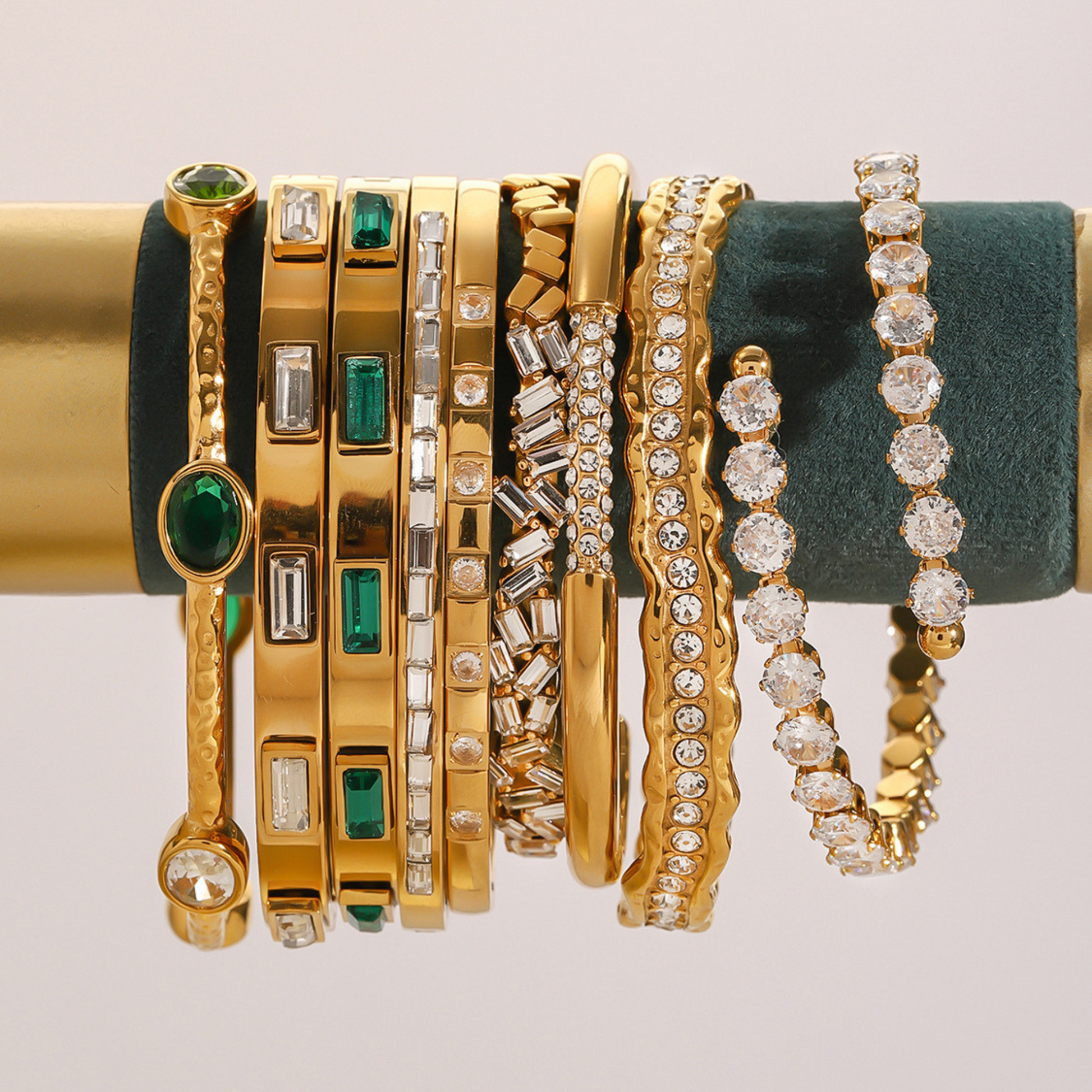 Collection of gold and diamond bracelets on a green velvet stand.