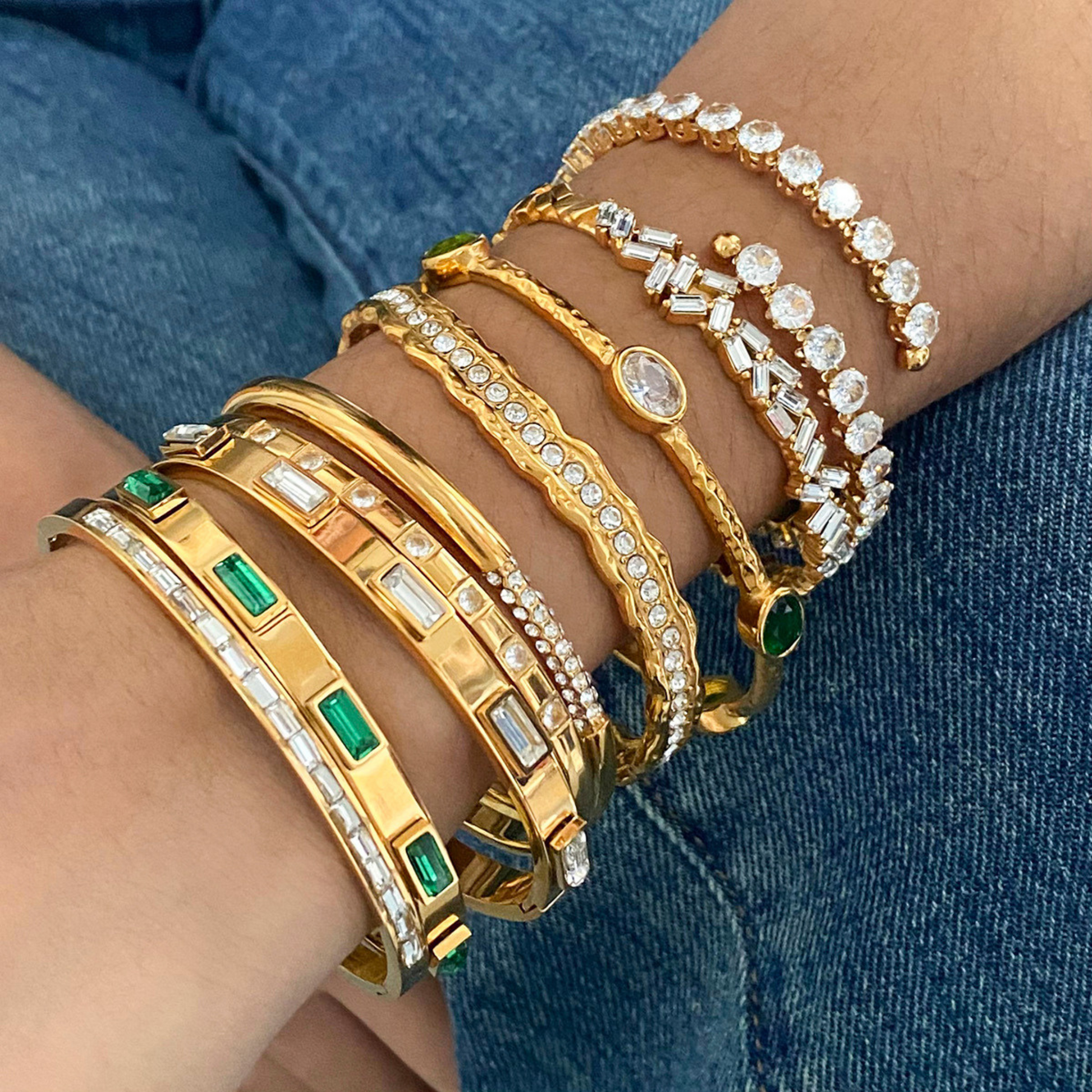 Gold and diamond bracelets on a person's wrist against a denim background