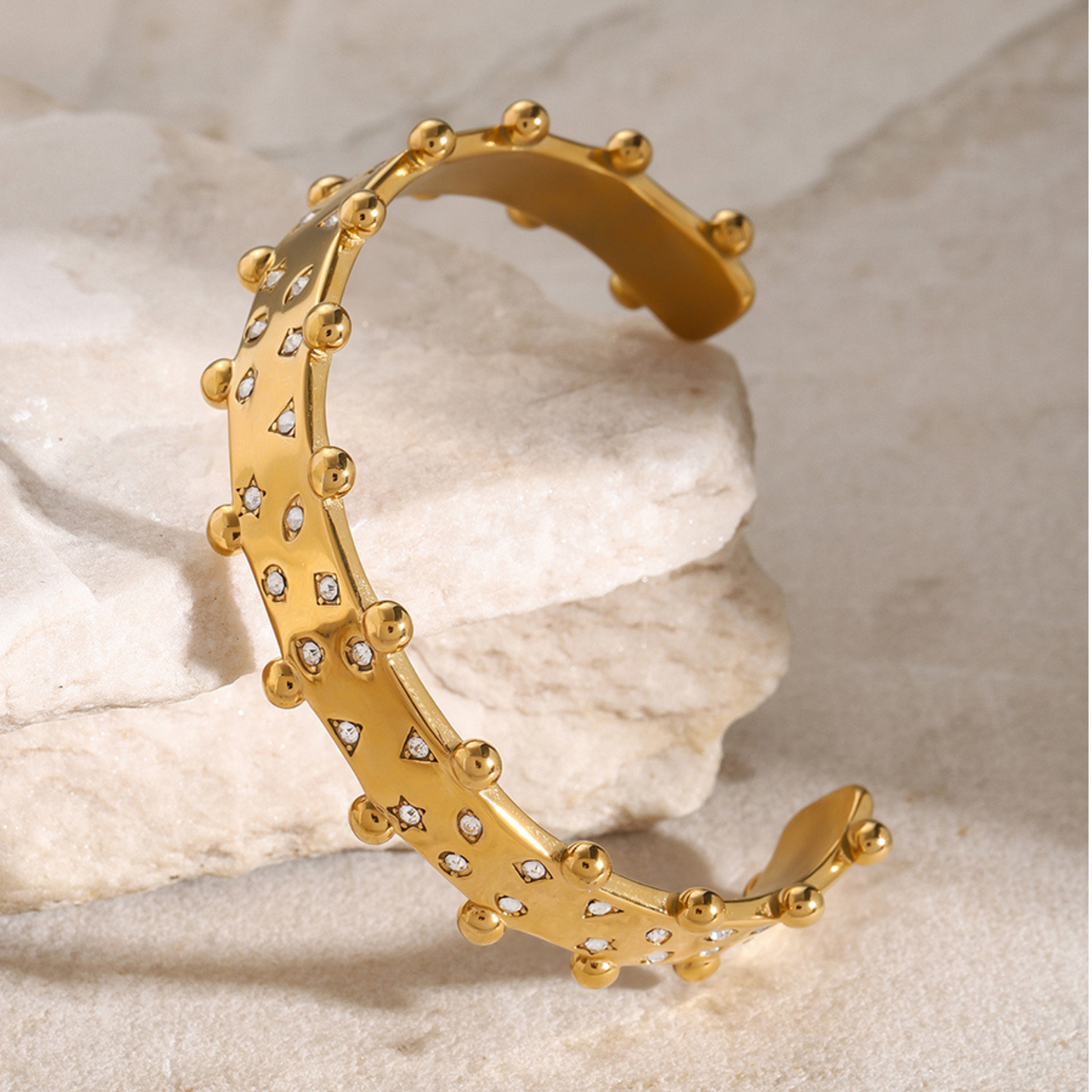 Gold bracelet with diamond accents on a beige stone background