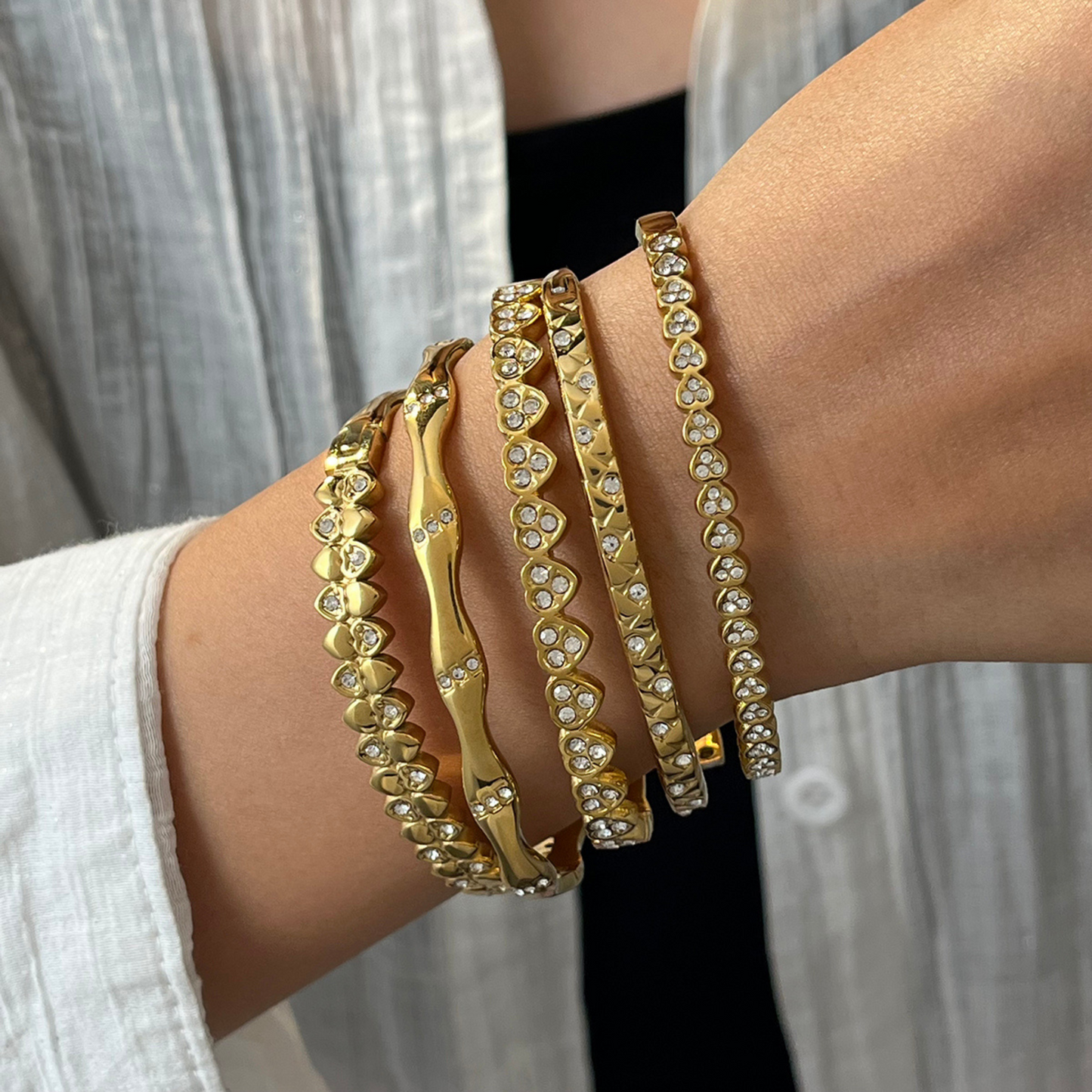 Gold bracelets with heart patterns on a wrist against a neutral background