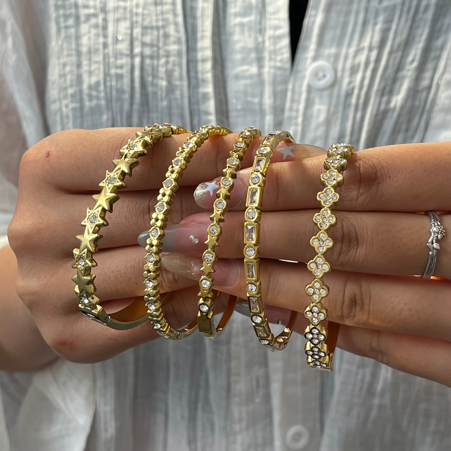 Gold bracelets with star and floral designs held by a person against a neutral background