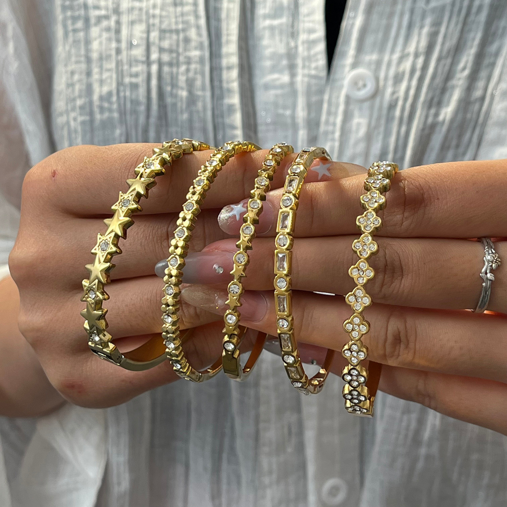 Gold bracelets with star and floral designs held by a person against a neutral background