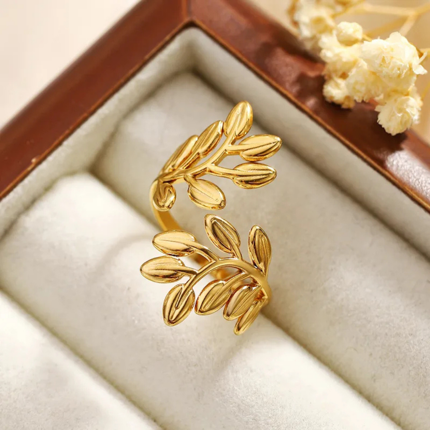 Gold leaf-shaped earring in a jewelry box with flowers in the background