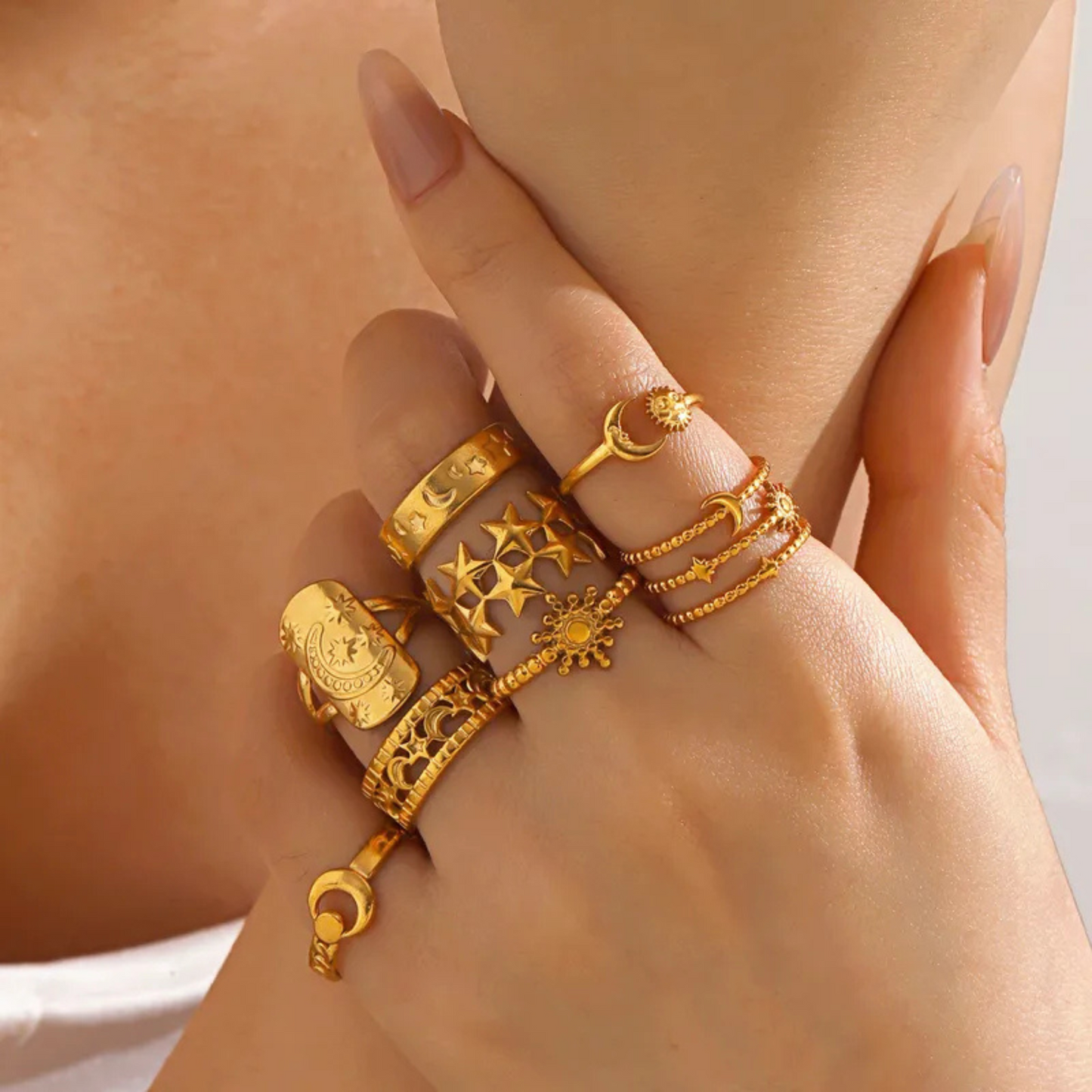 Hand wearing multiple gold rings with intricate designs on a neutral background