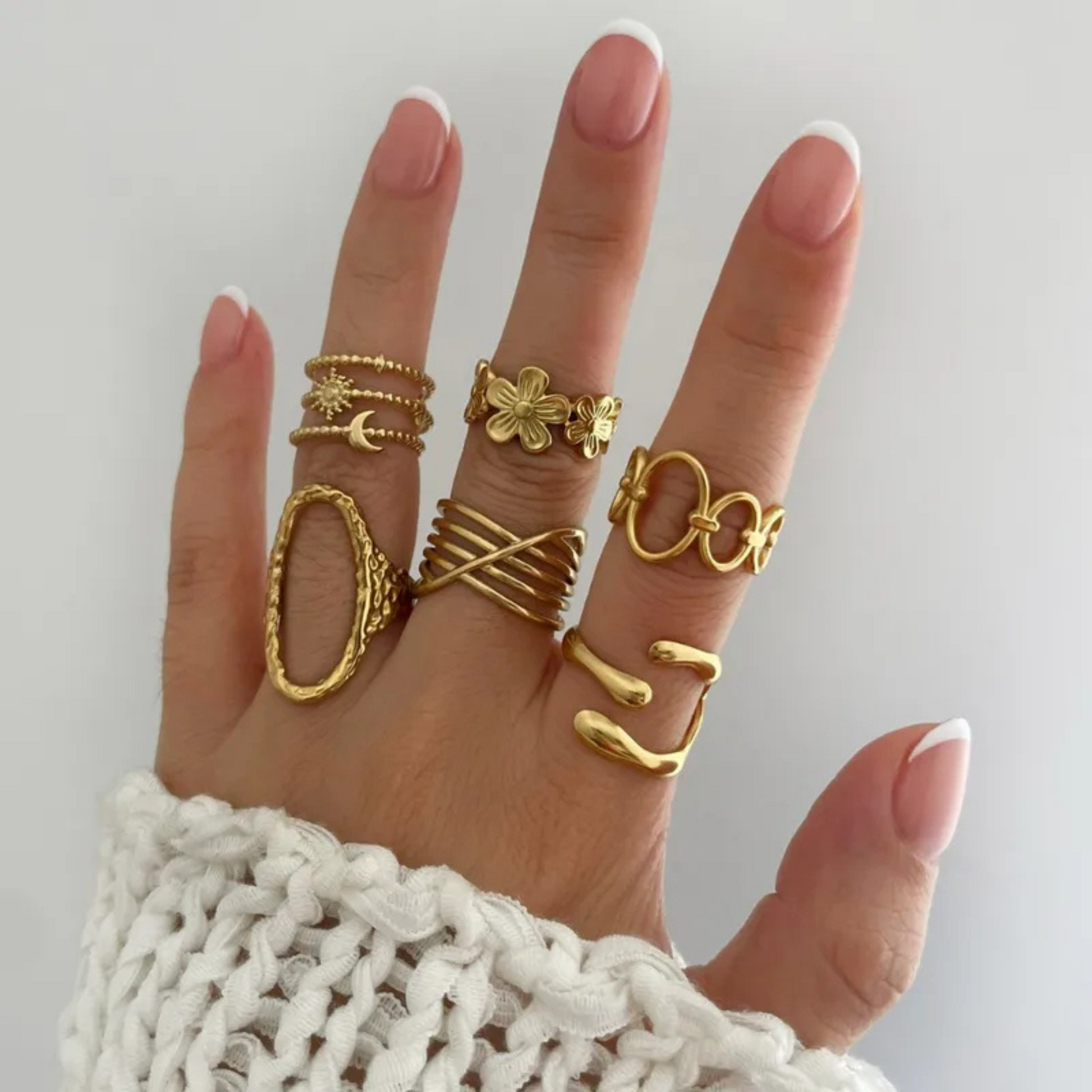 Hand wearing multiple gold rings on a plain background