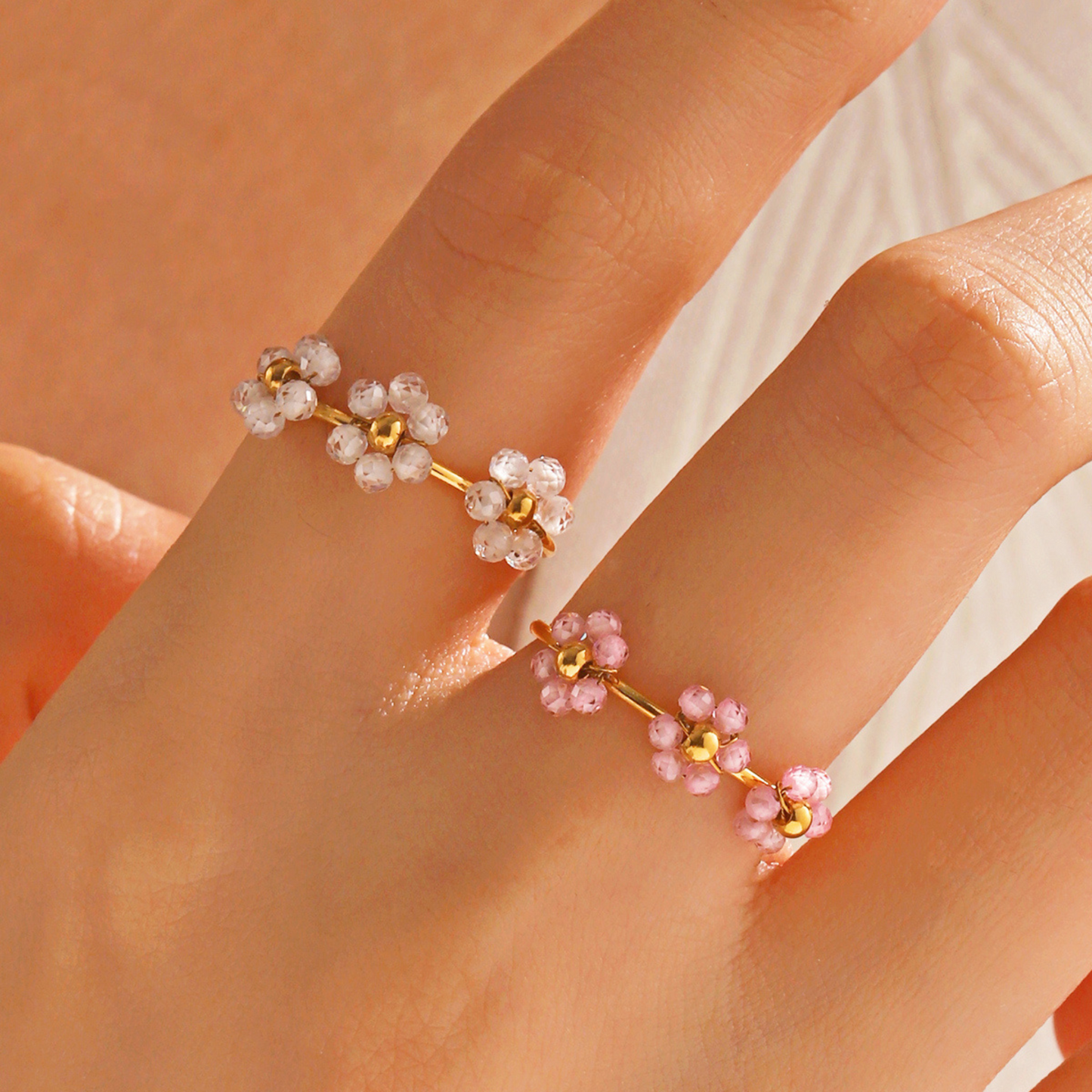 Gold and pink floral earrings on a hand against a neutral background