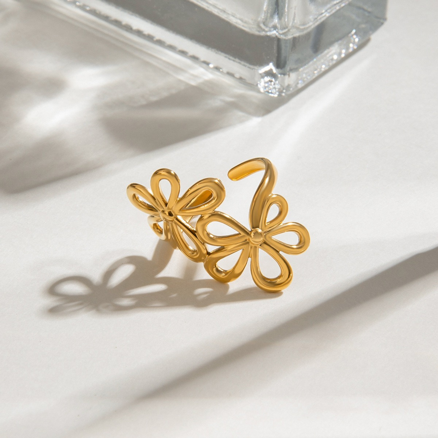 Gold floral earrings on a white surface with a clear crystal object in the background