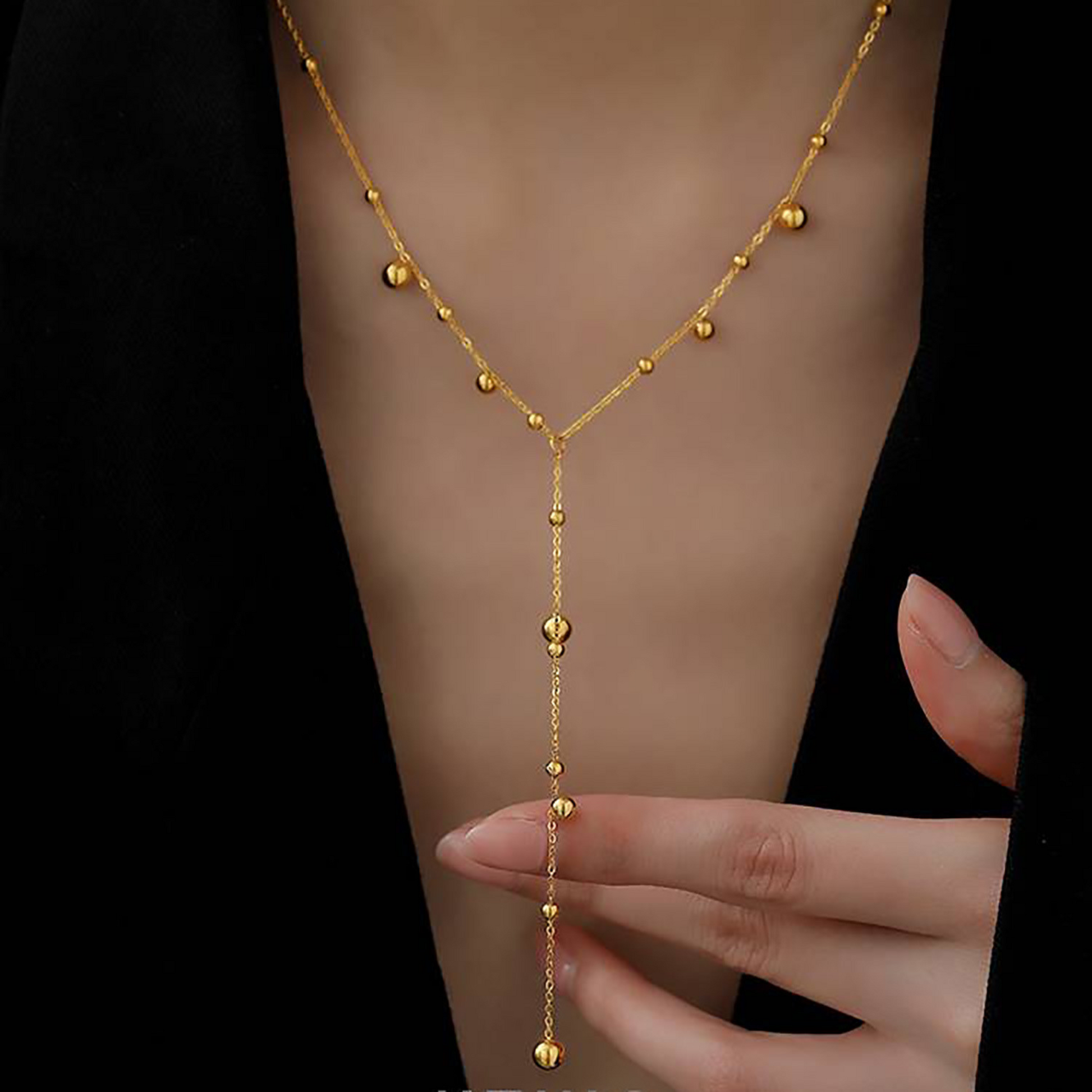 Gold body chain worn on a person's arm with a black background