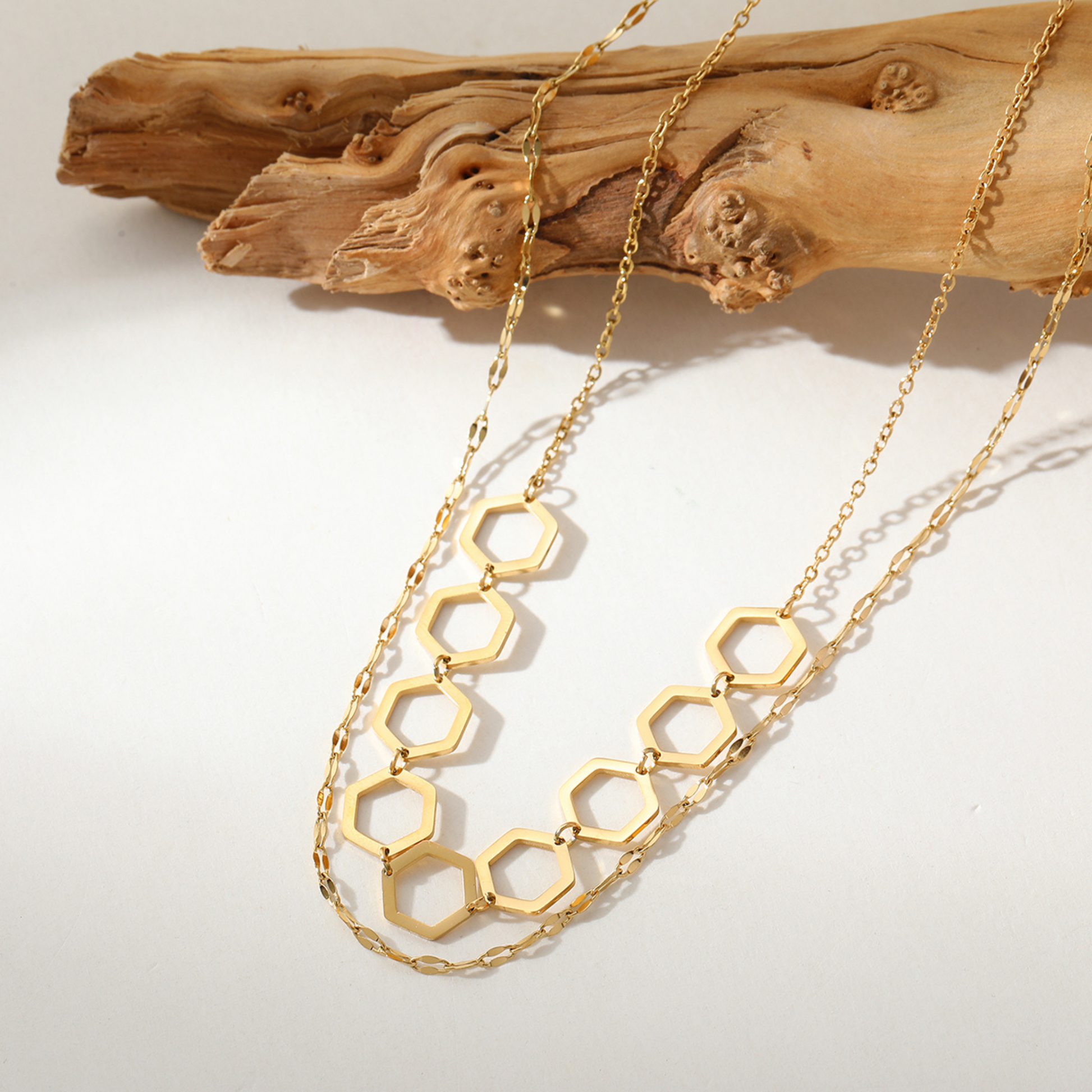 Gold hexagonal chain necklace on a light background with wooden texture
