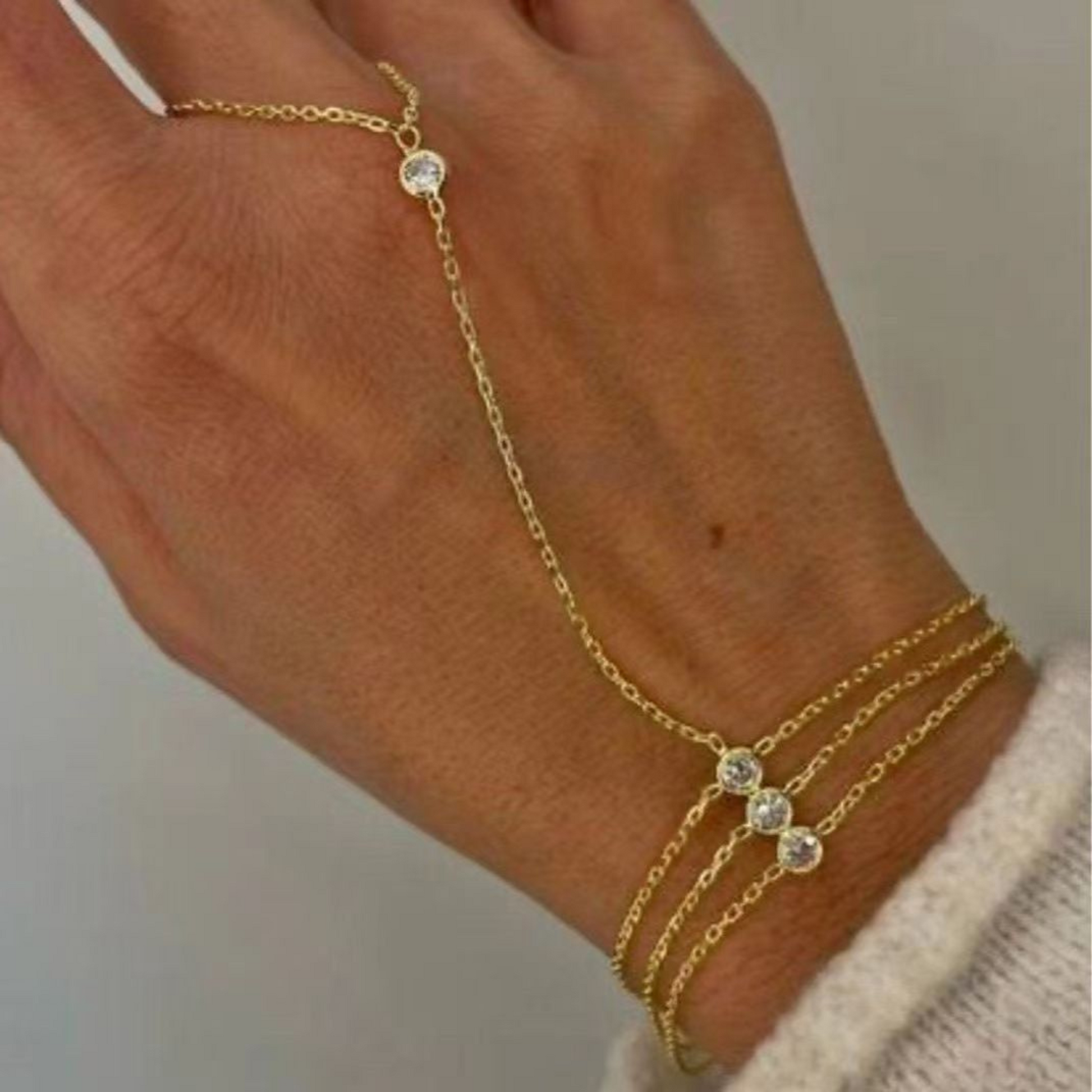 Gold ring bracelet with small gemstones on a wrist against a neutral background
