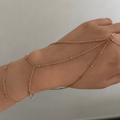 Hand wearing multiple gold ring chain bracelets on a neutral background
