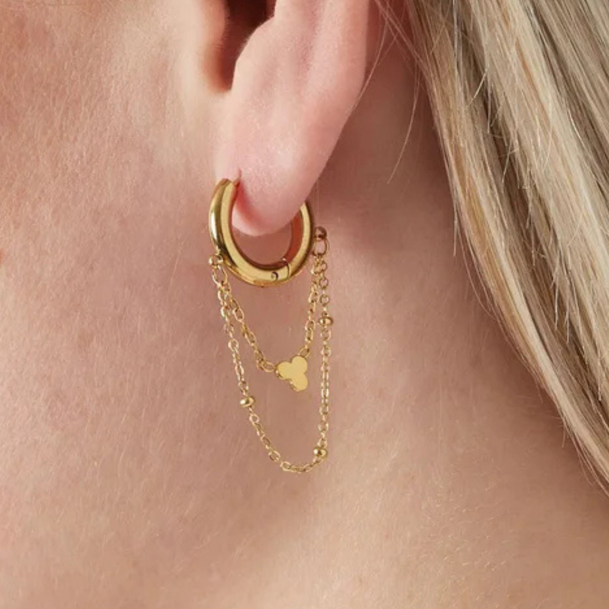 Gold hoop earring with chain detail worn by a person