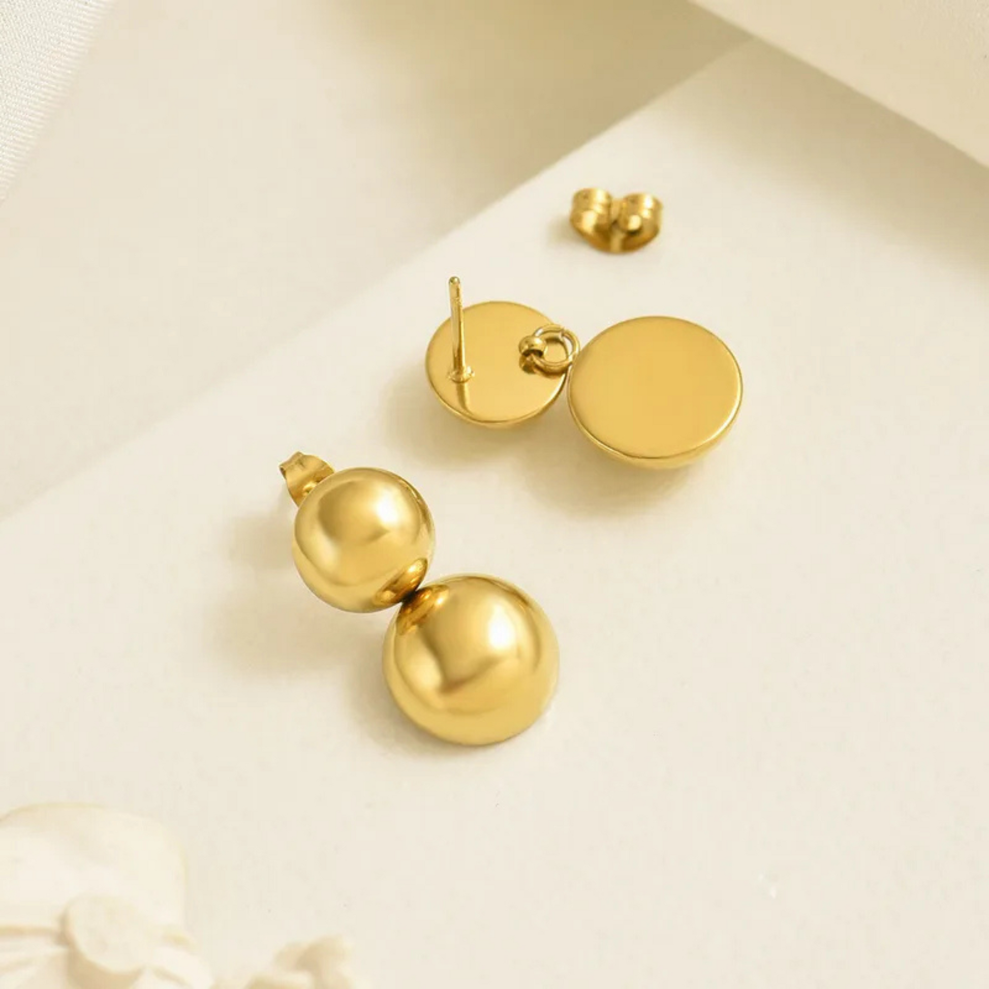 Gold ball earrings on a beige background