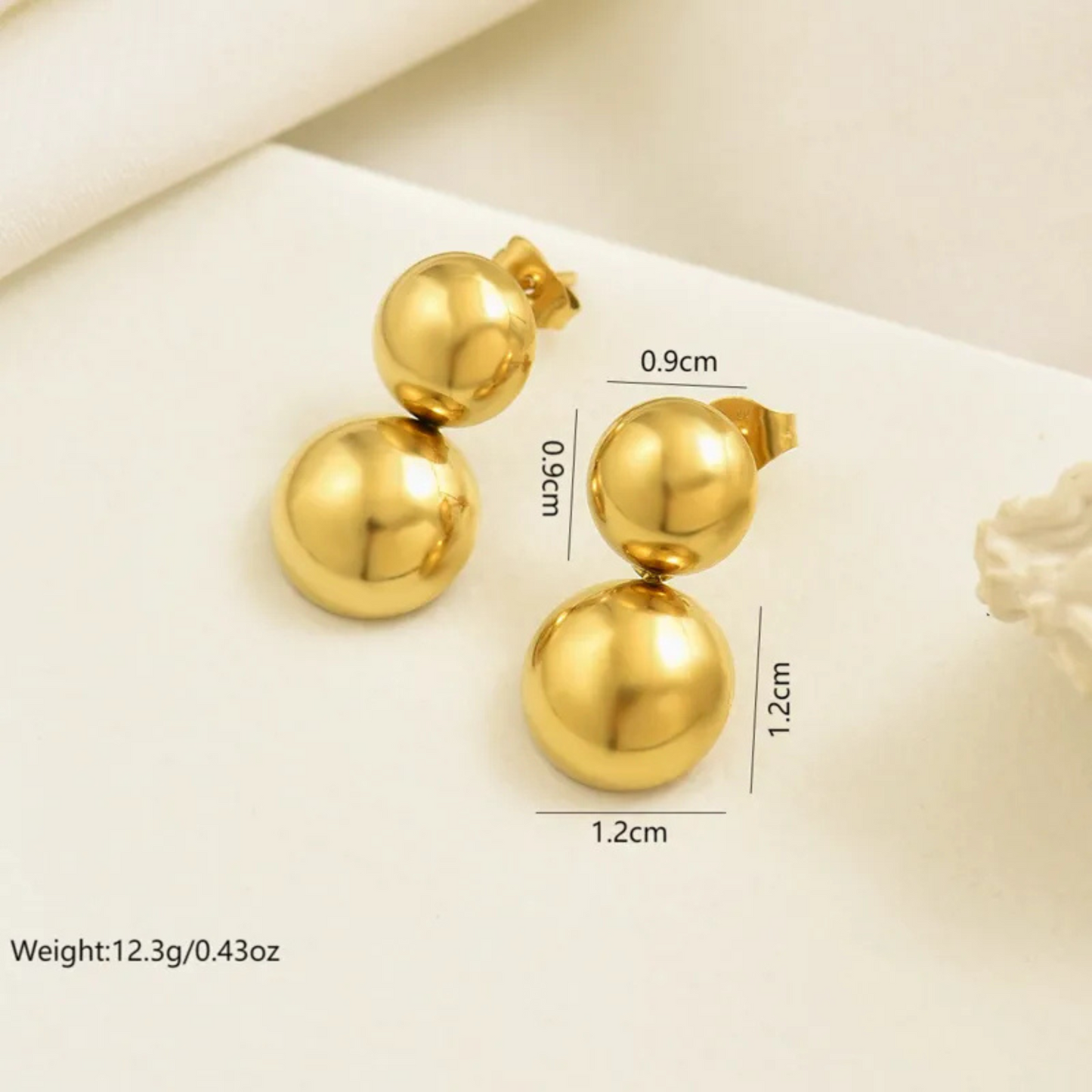 Gold earrings with measurements on a light background