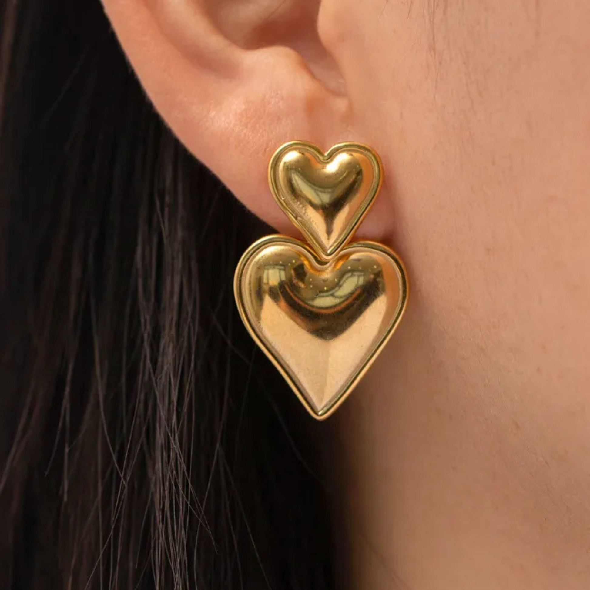 Gold heart-shaped earrings worn by a person with dark hair.