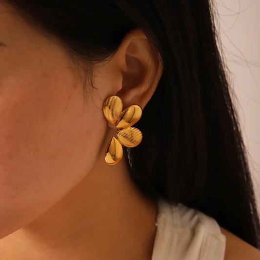 Close-up of a person wearing gold flower-shaped earrings.