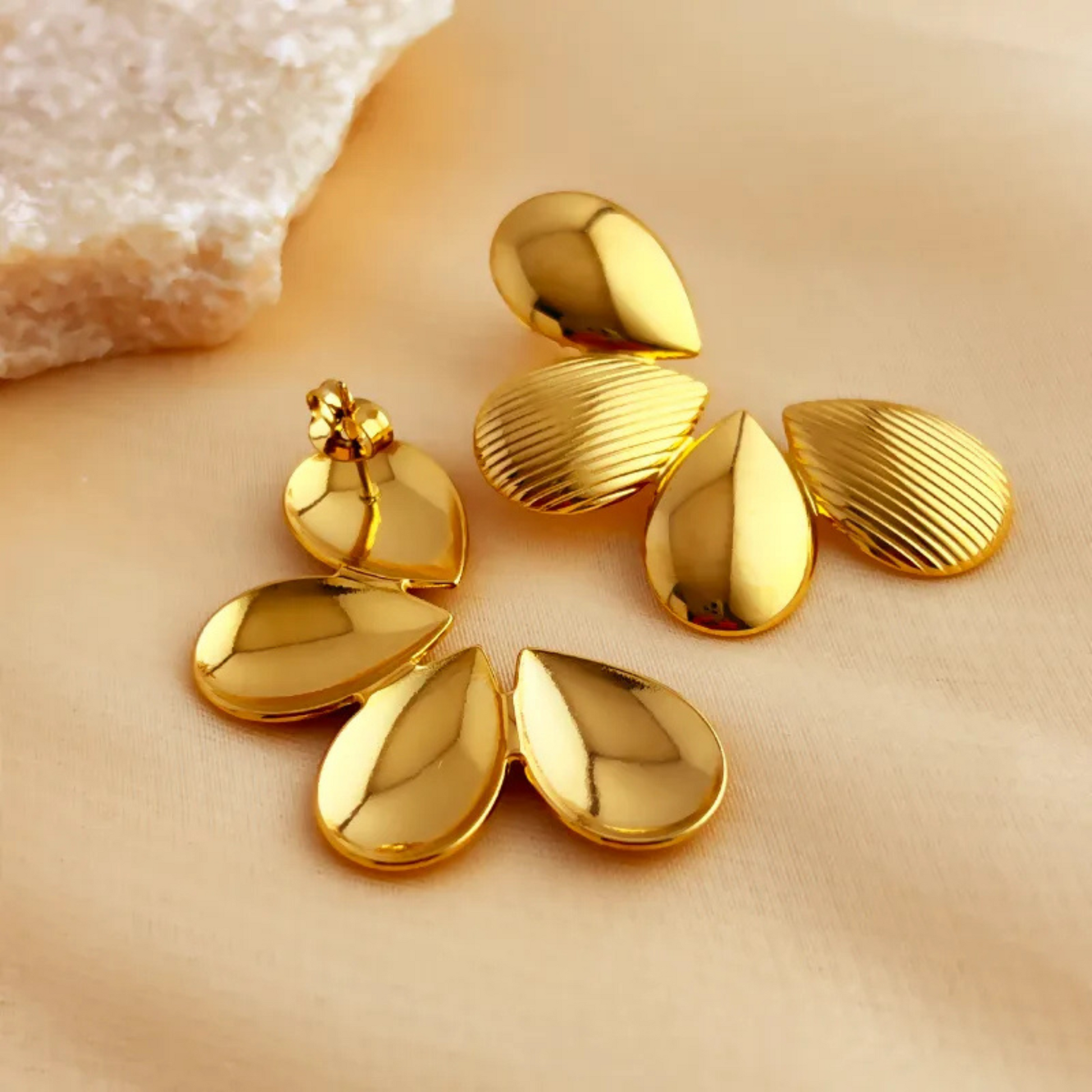 Gold leaf-shaped earrings on a beige surface