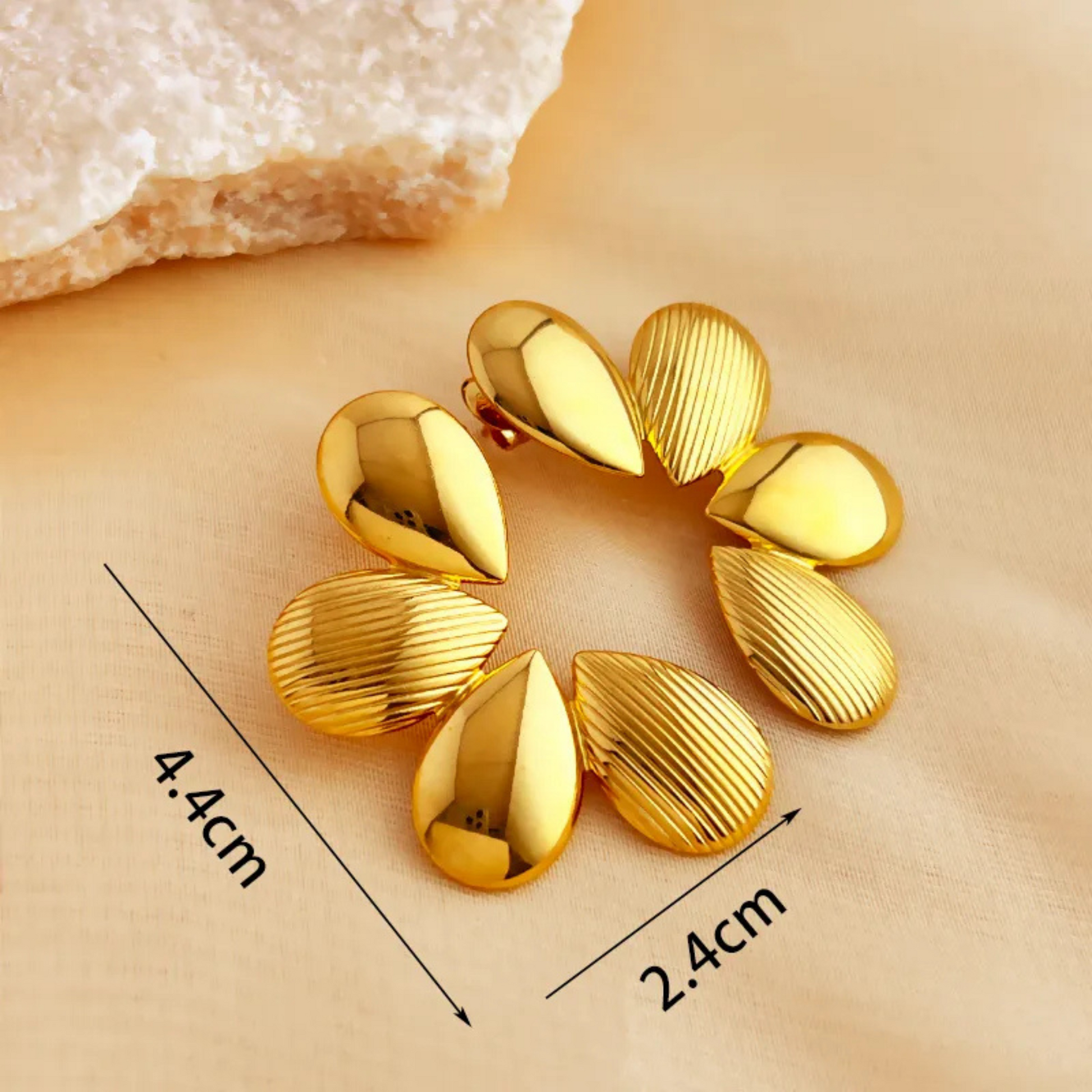 Gold earrings with measurements on a beige background