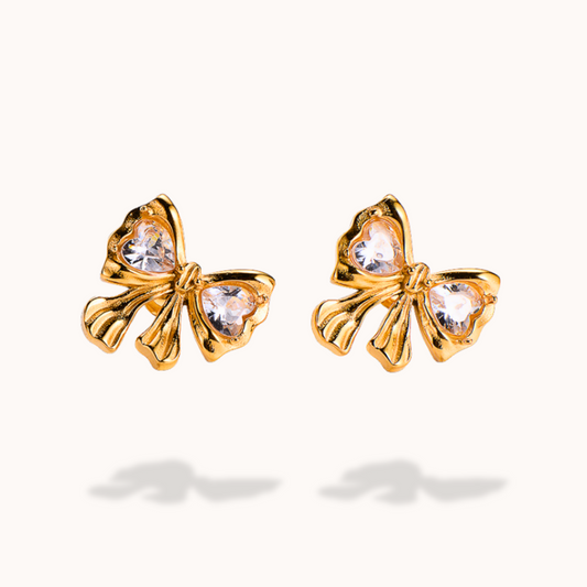 Gold bow-shaped earrings with clear gemstones on a white background
