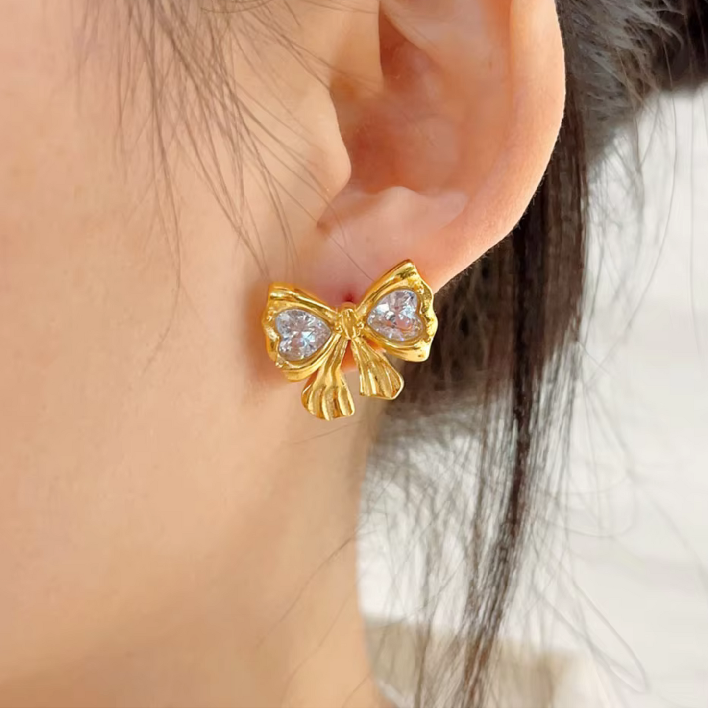 Gold bow-shaped earring worn on an ear with a blurred background